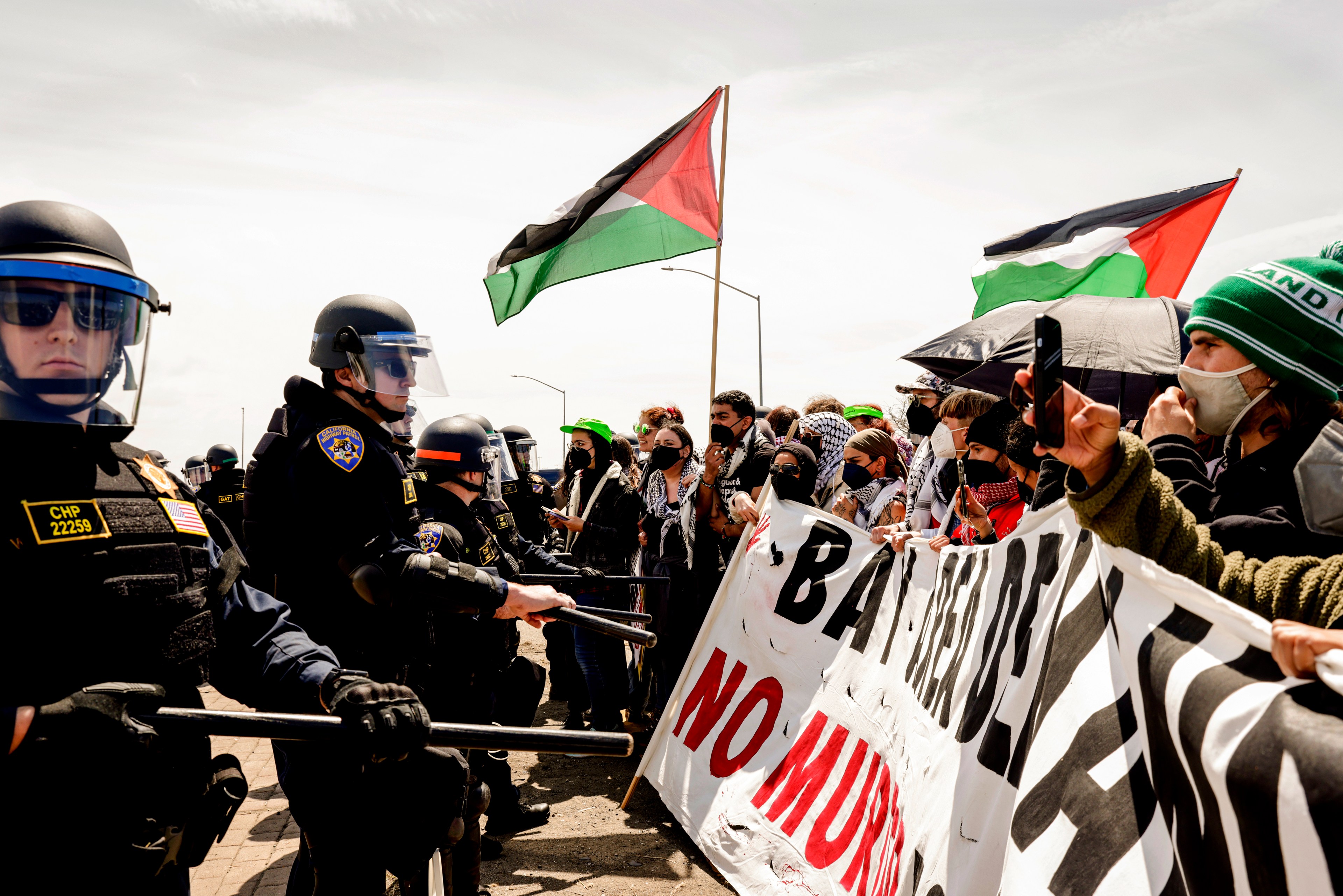 Riot police face off with protesters holding banners and a Palestinian flag.
