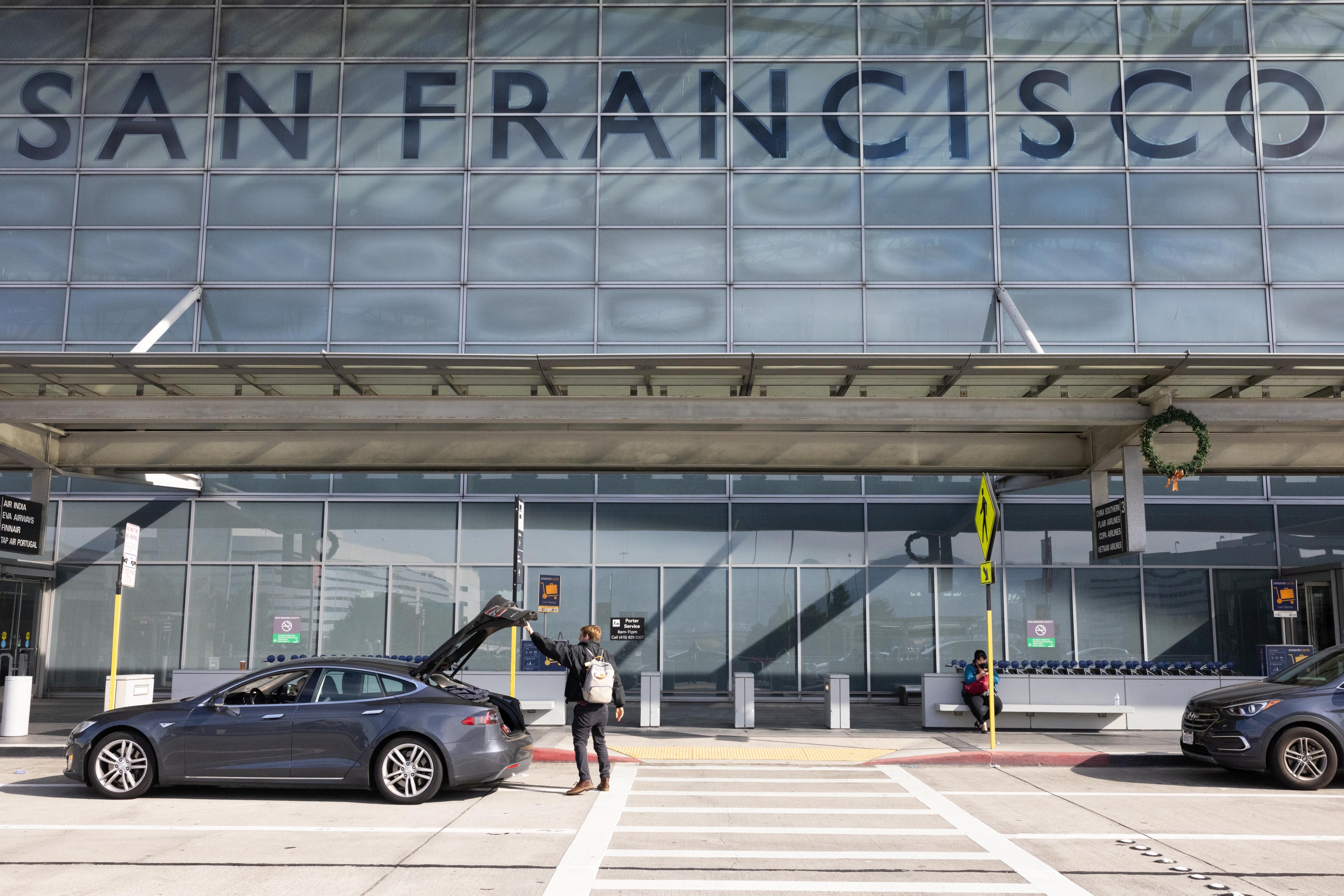 A man loads luggage into a car by an airport.