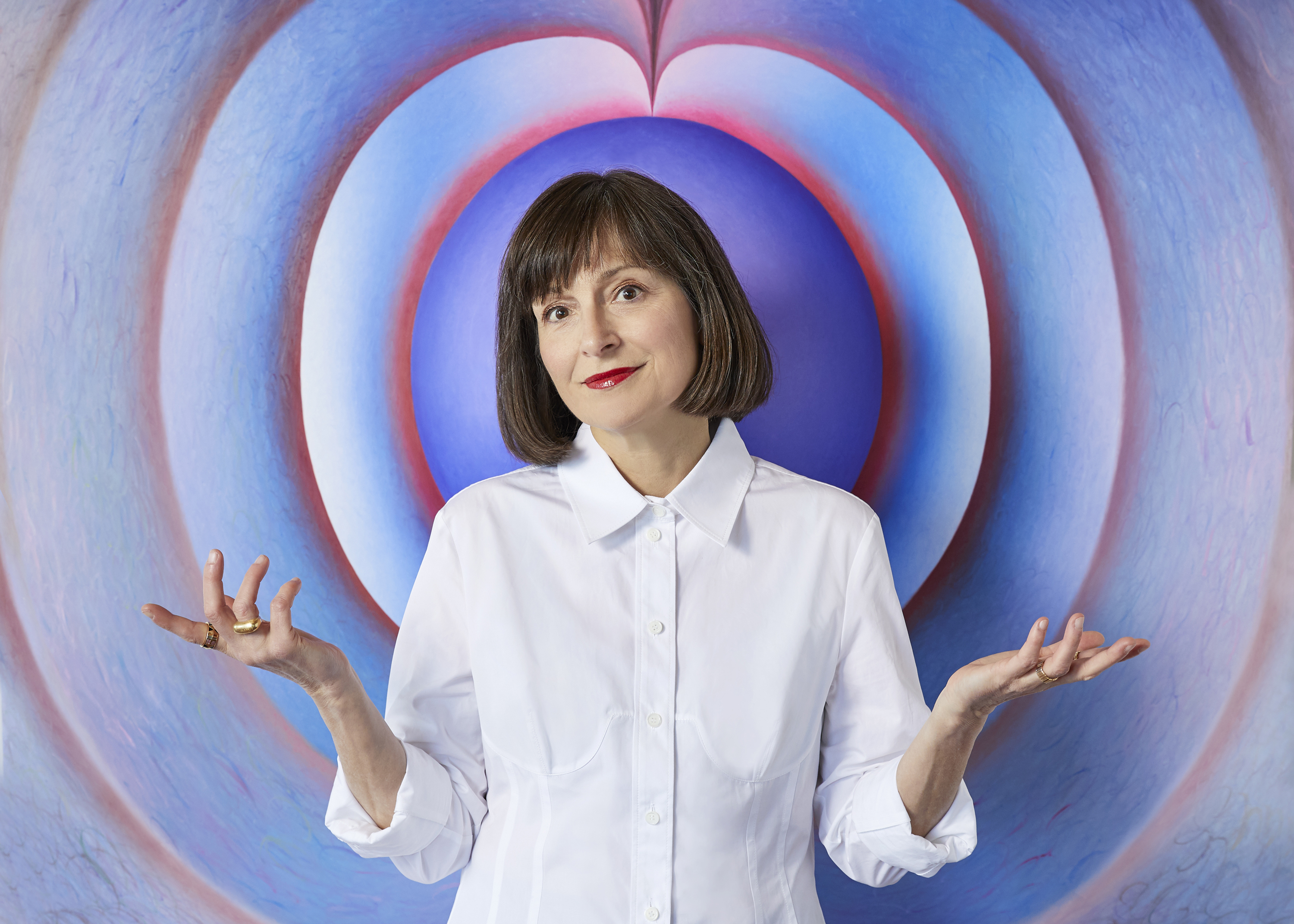 A woman in a white shirt gestures with a whimsical look against a colorful swirl backdrop.