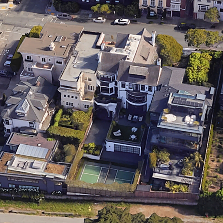 Aerial view of a luxury house with multiple terraces, a pickleball court, and a rooftop garden, surrounded by other homes.