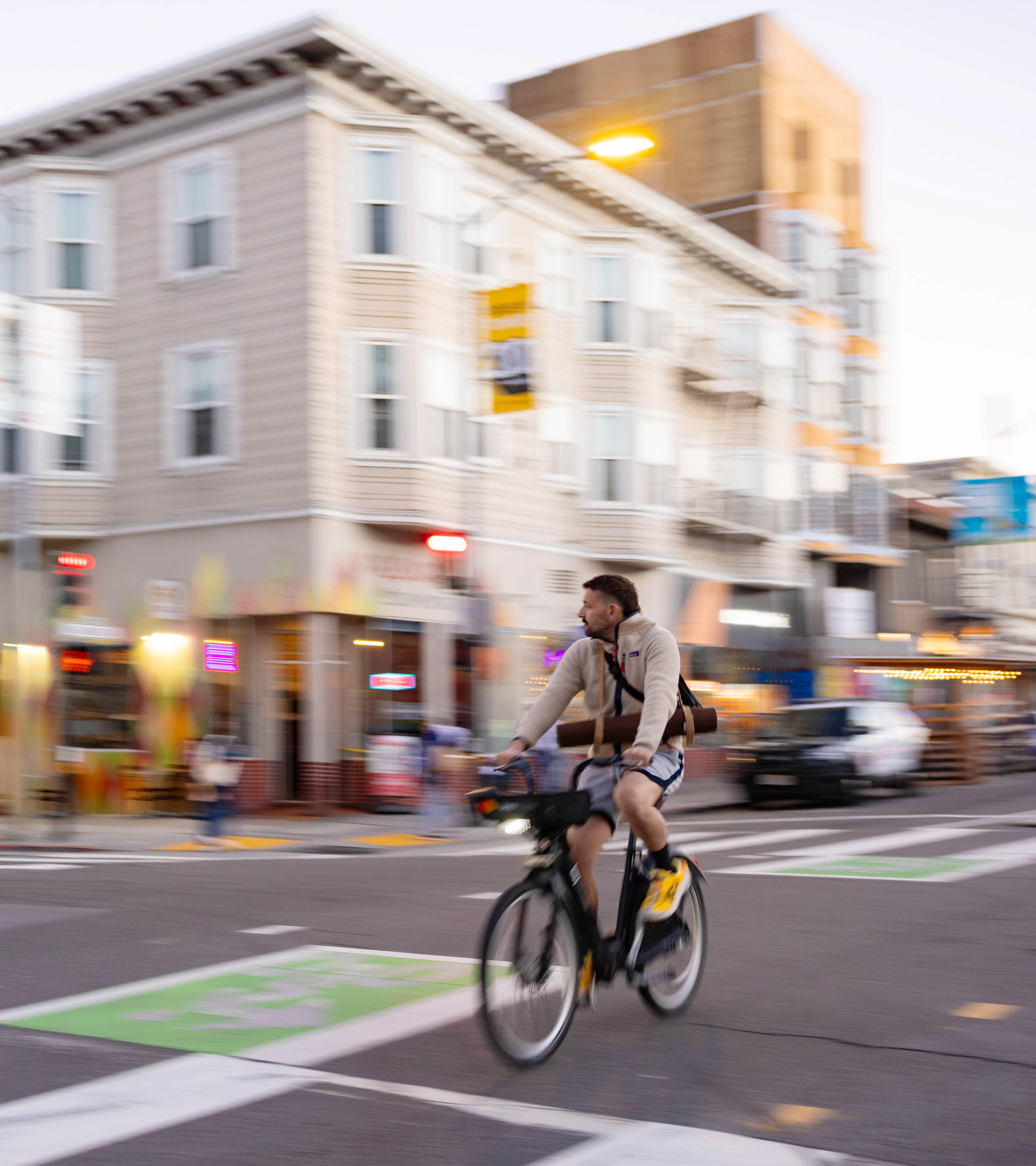 A blurred image of a person riding a bike across a city street intersection.