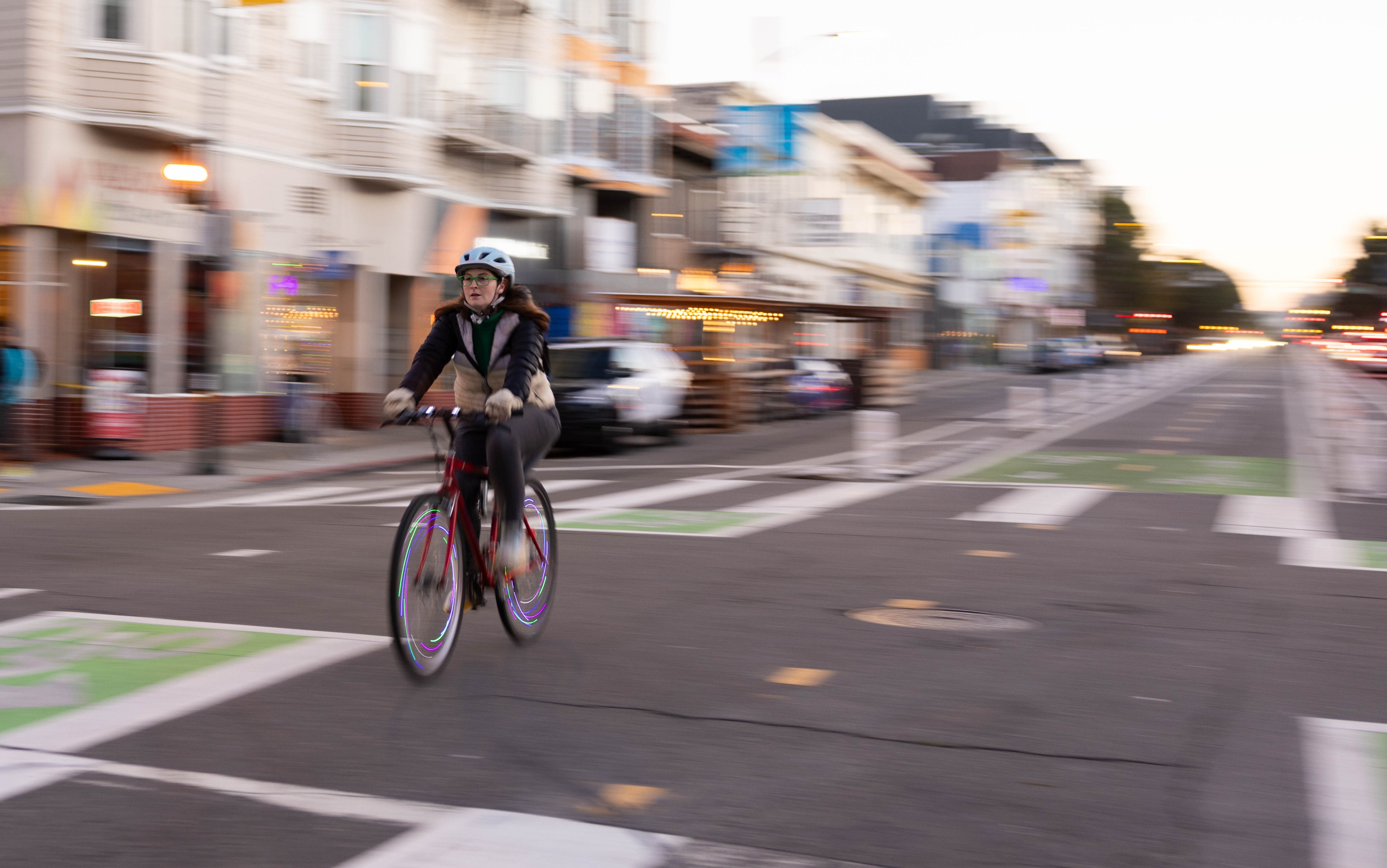 A person cycling on a city street at dusk, motion blur emphasizes their movement.