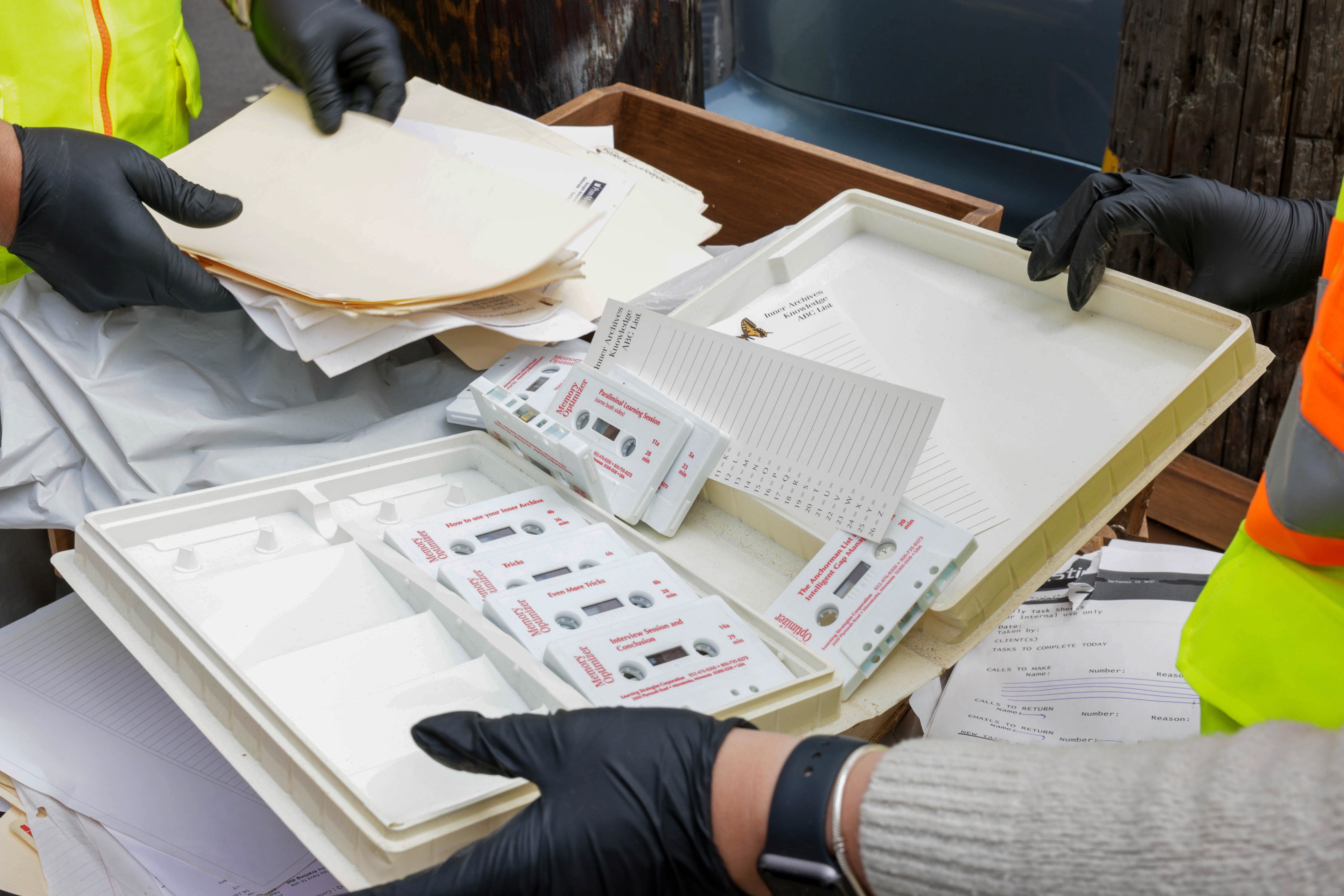 Workers in gloves handle documents and tests near a dumpster.