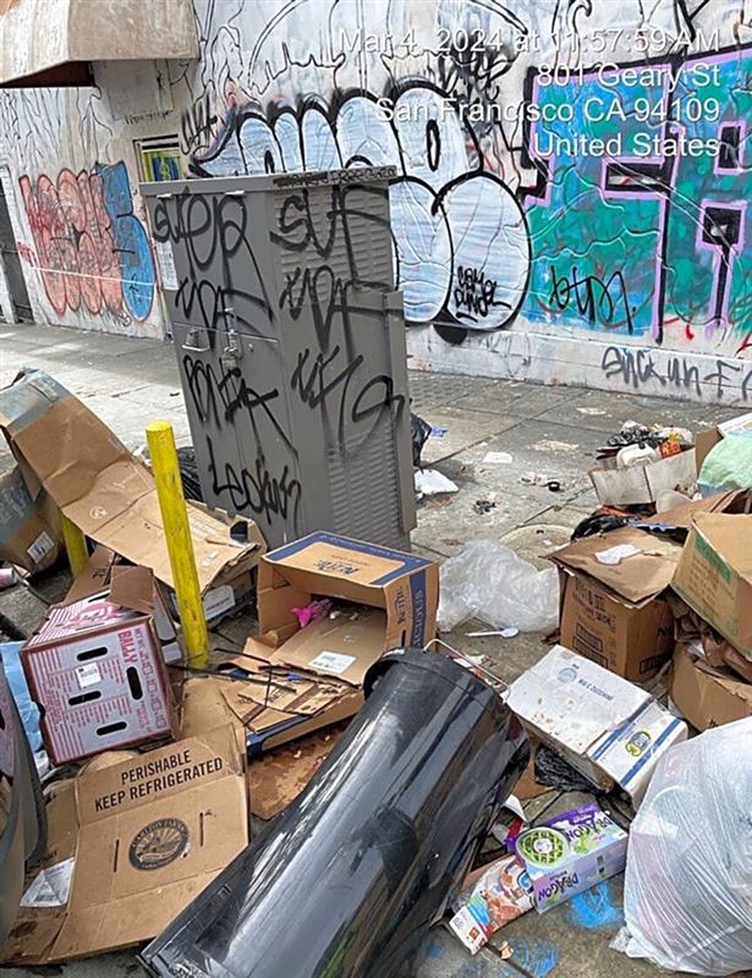 An alleyway littered with trash and boxes, with graffiti-covered walls and a utility box.