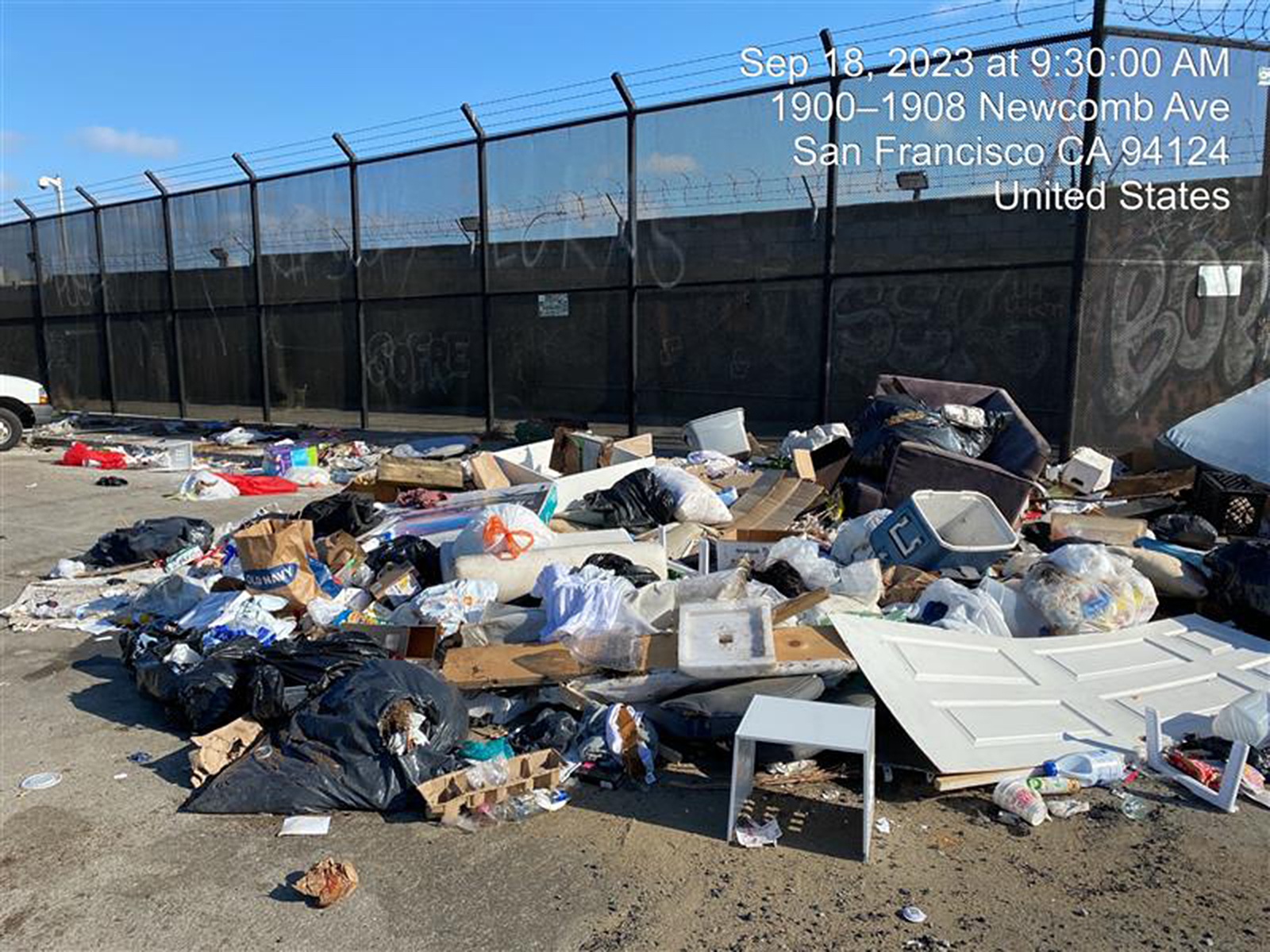 A large, messy pile of trash strewn across an urban lot with graffiti-covered walls.