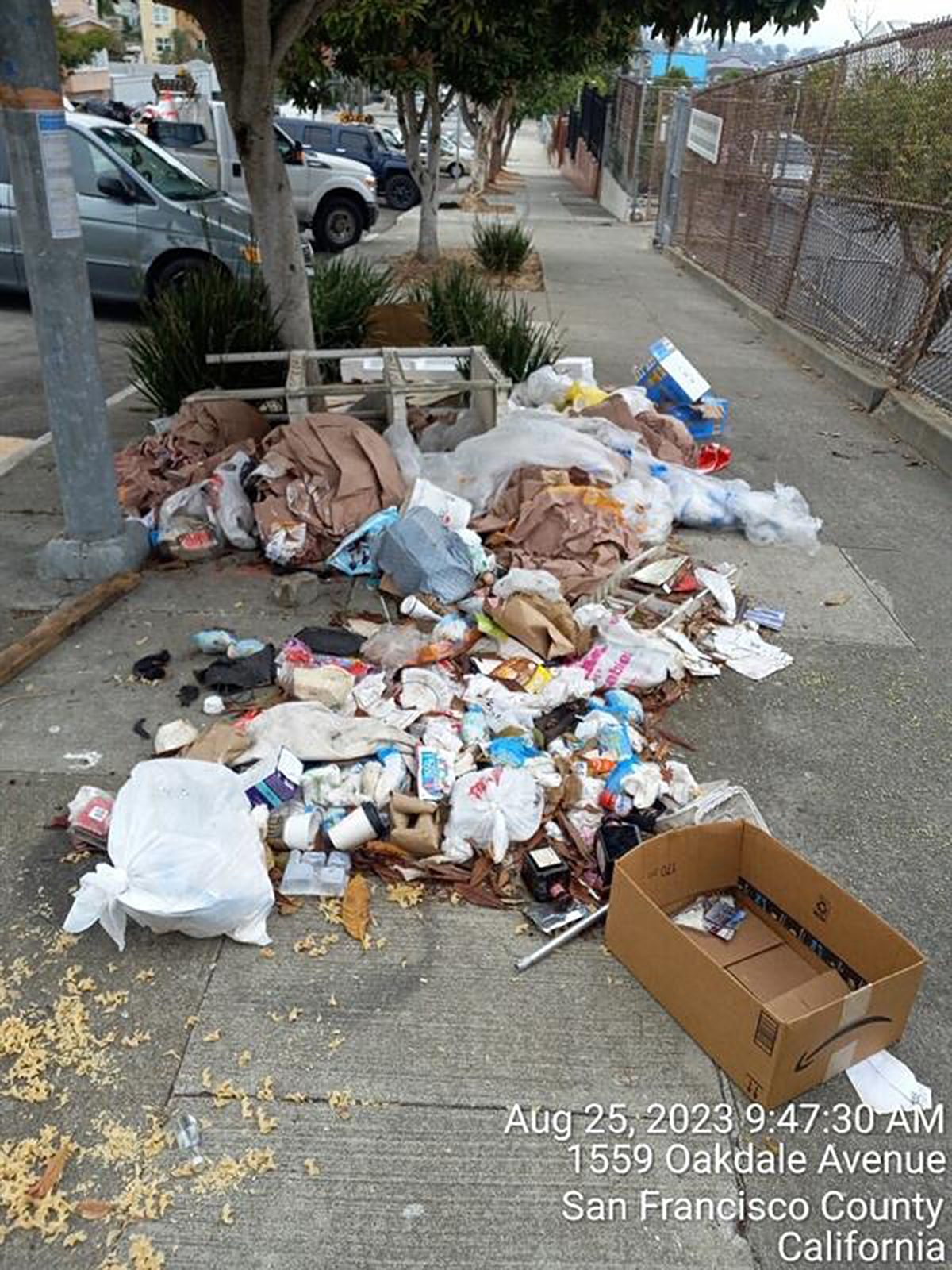 A sidewalk is cluttered with scattered trash and loose debris beside a street.