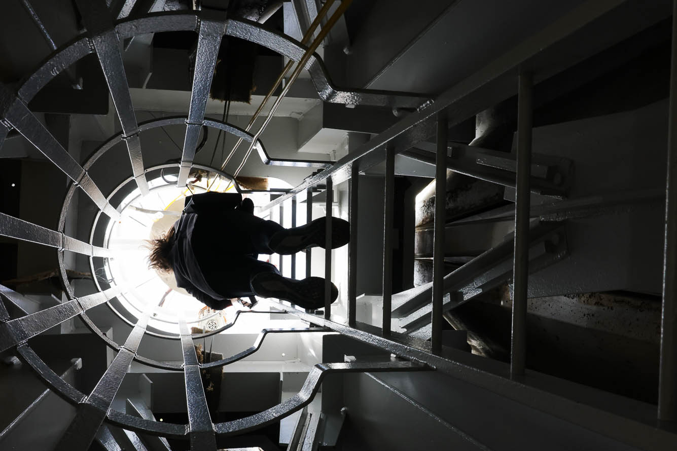 A person ascends a spiraling staircase inside a tower, illuminated from above.