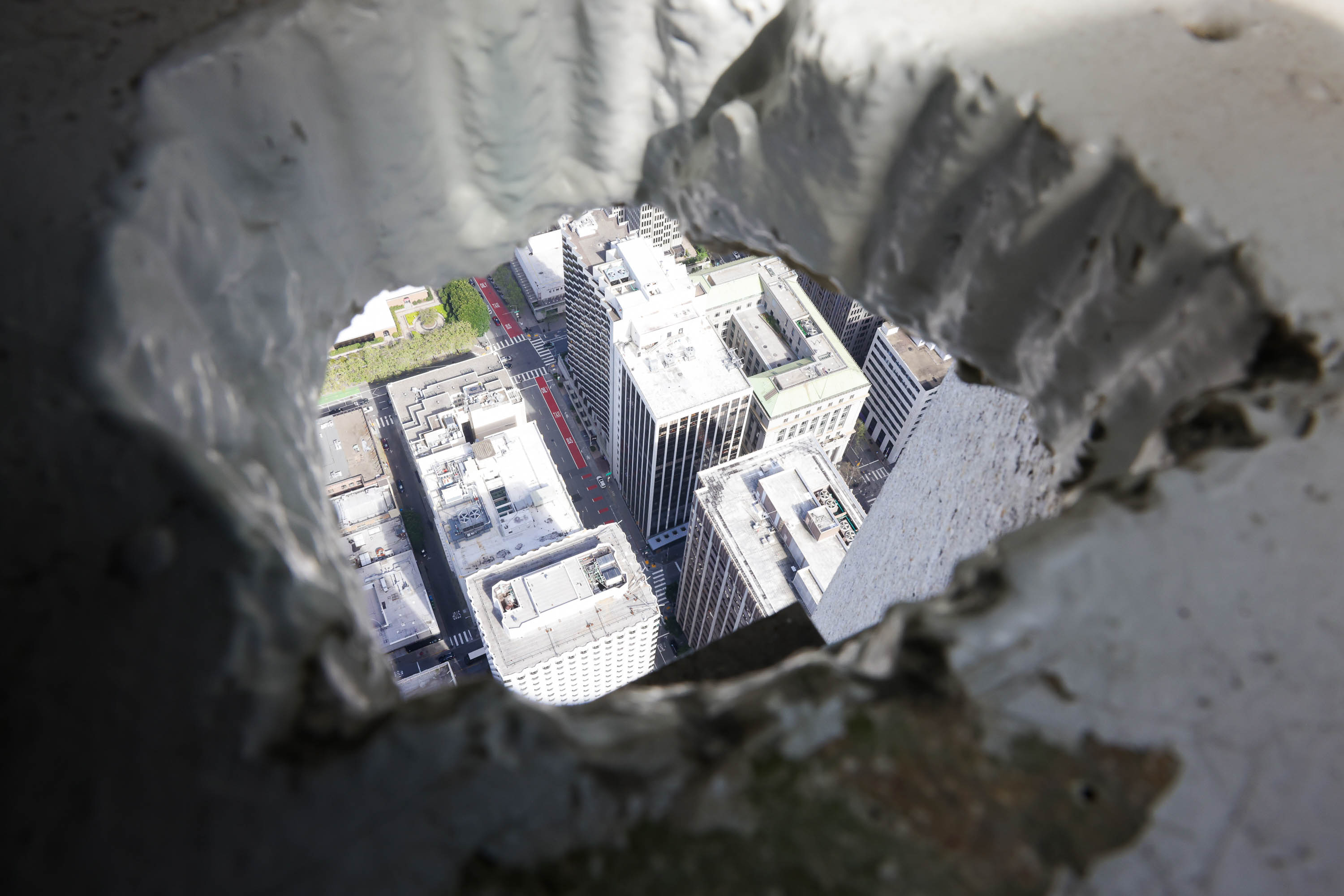 Aerial view of city buildings through a rough-edged hole in a structure.