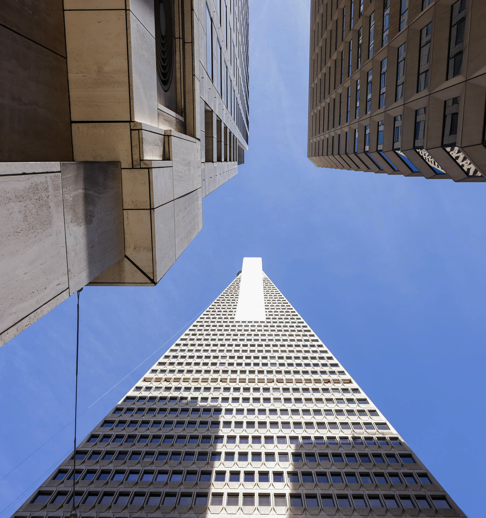 An upward view between high-rises towards a clear blue sky, showcasing contrasting building architectures.