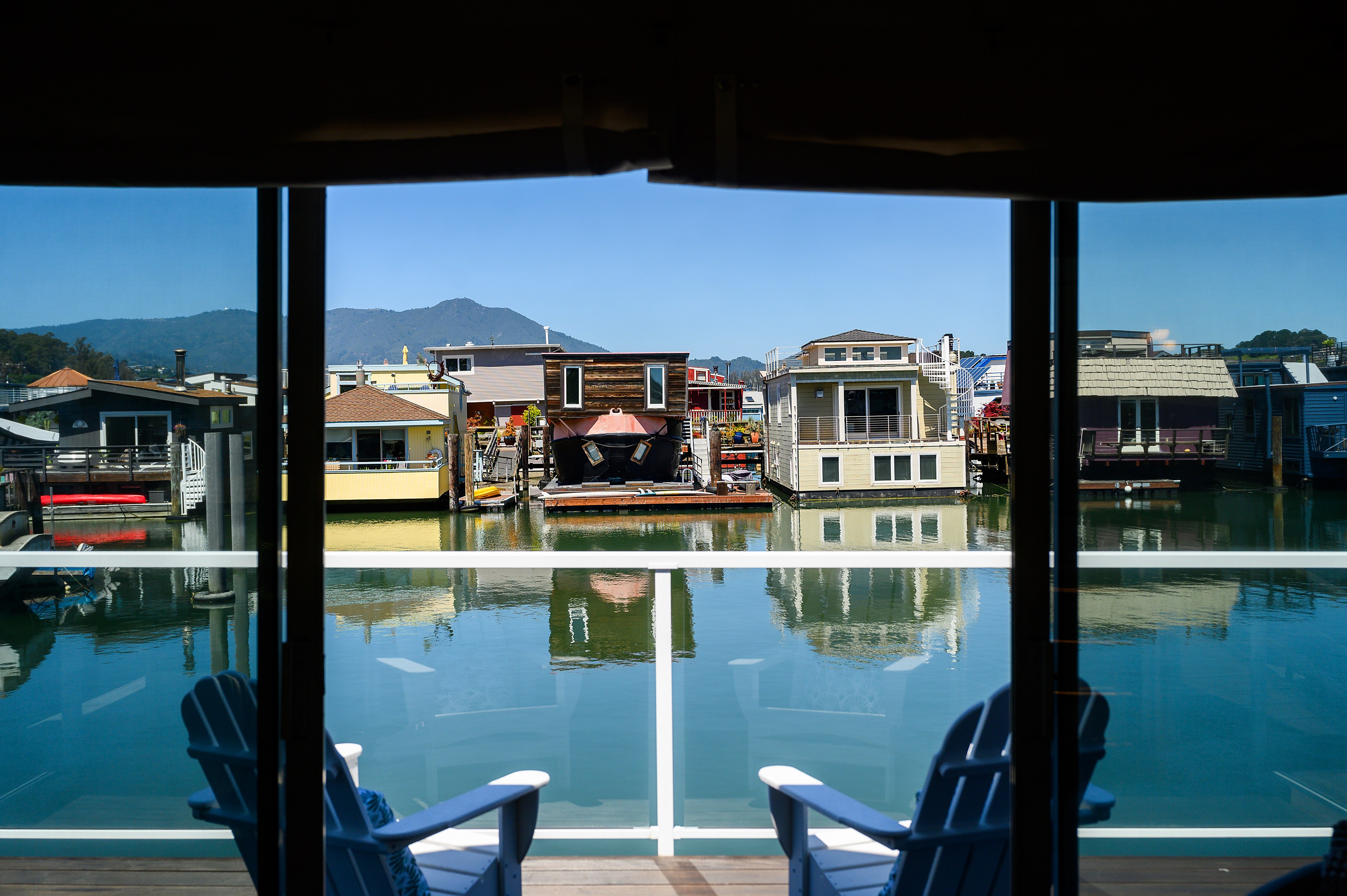 View from a balcony with chairs, overlooking colorful floating houses and calm water, with mountains in the distance.