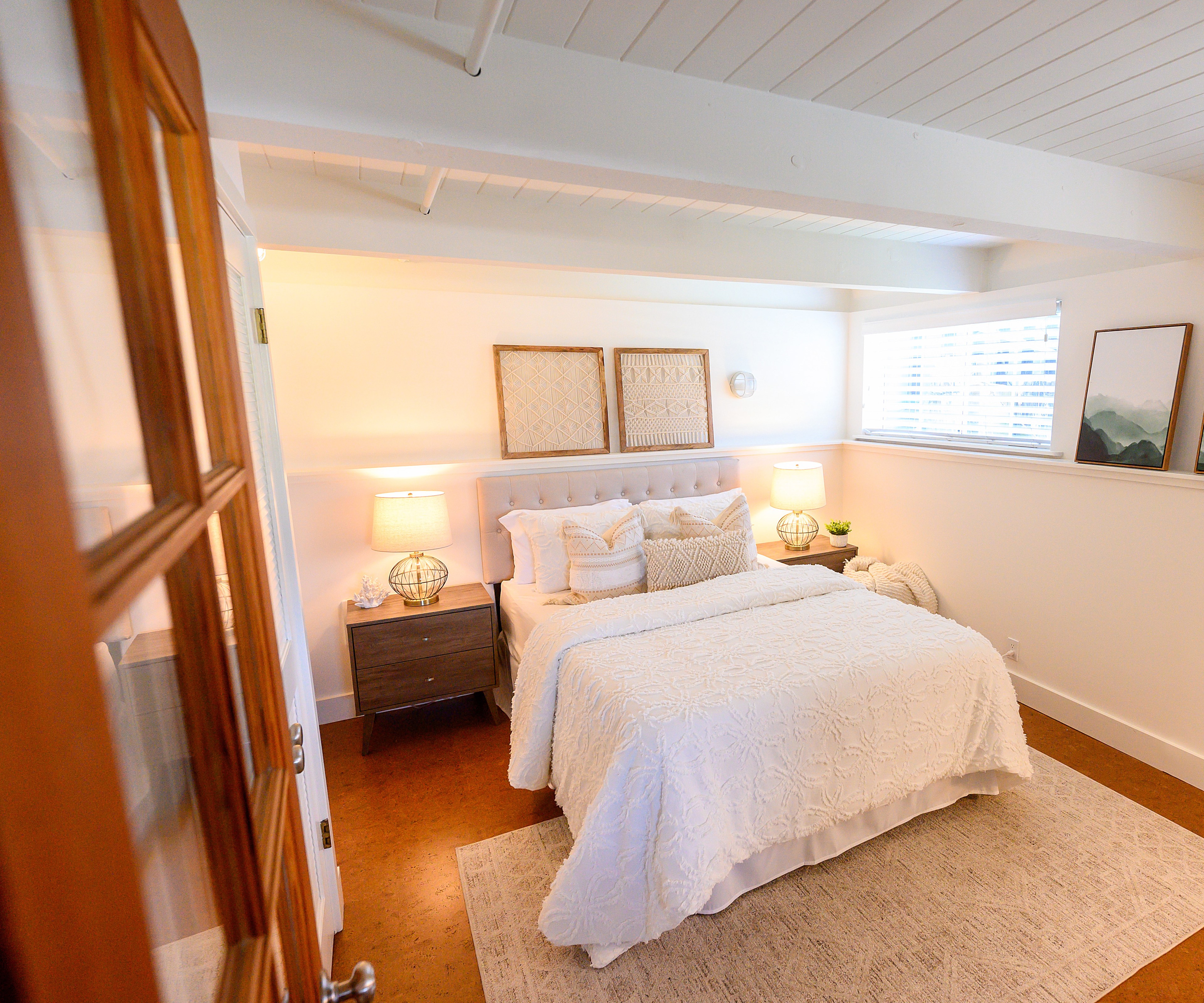 A cozy, well-lit bedroom with a white bed, two nightstands with lamps, and decorative art.