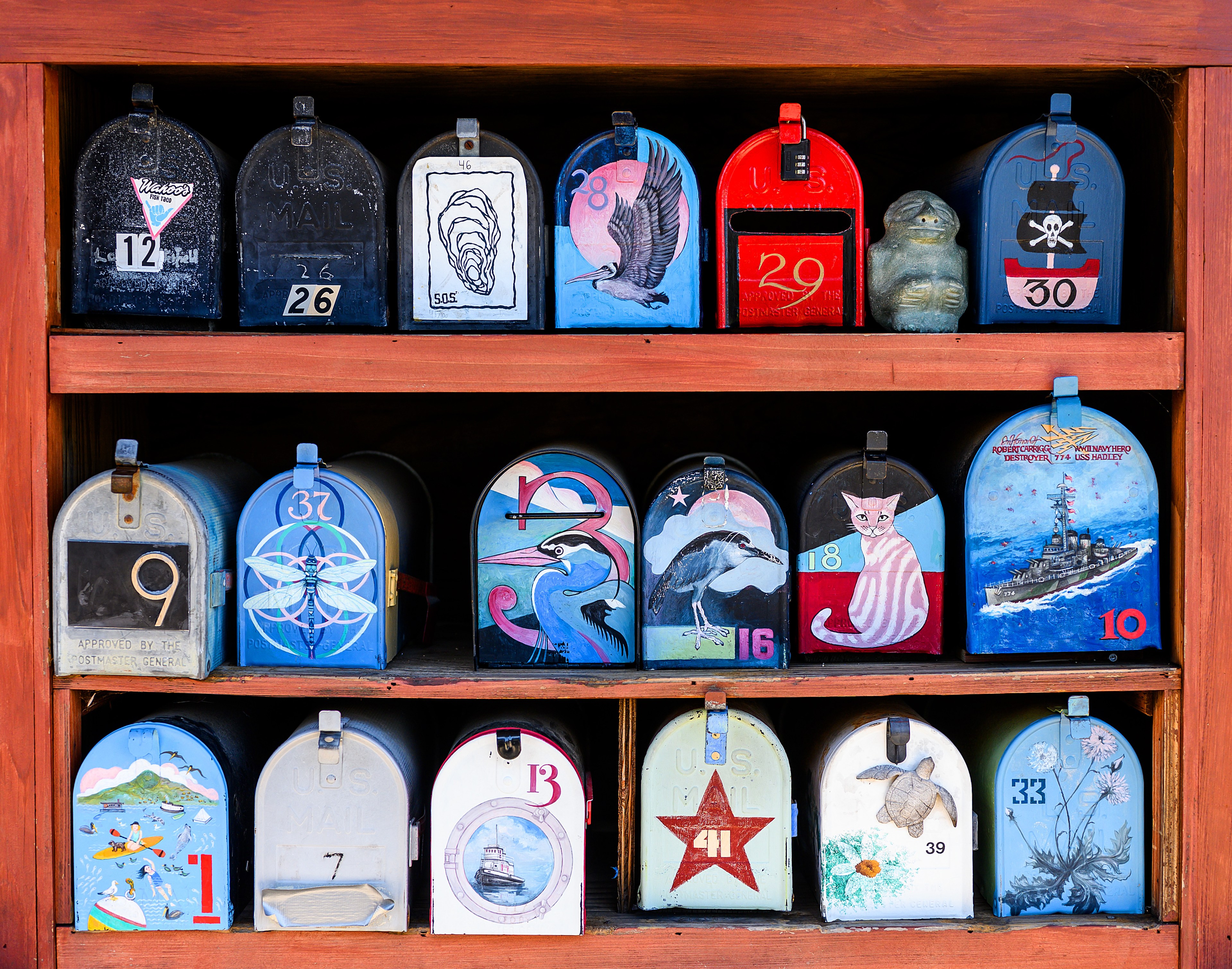 A collection of uniquely painted mailboxes displayed on shelves, each featuring different designs, colors, and numbers.