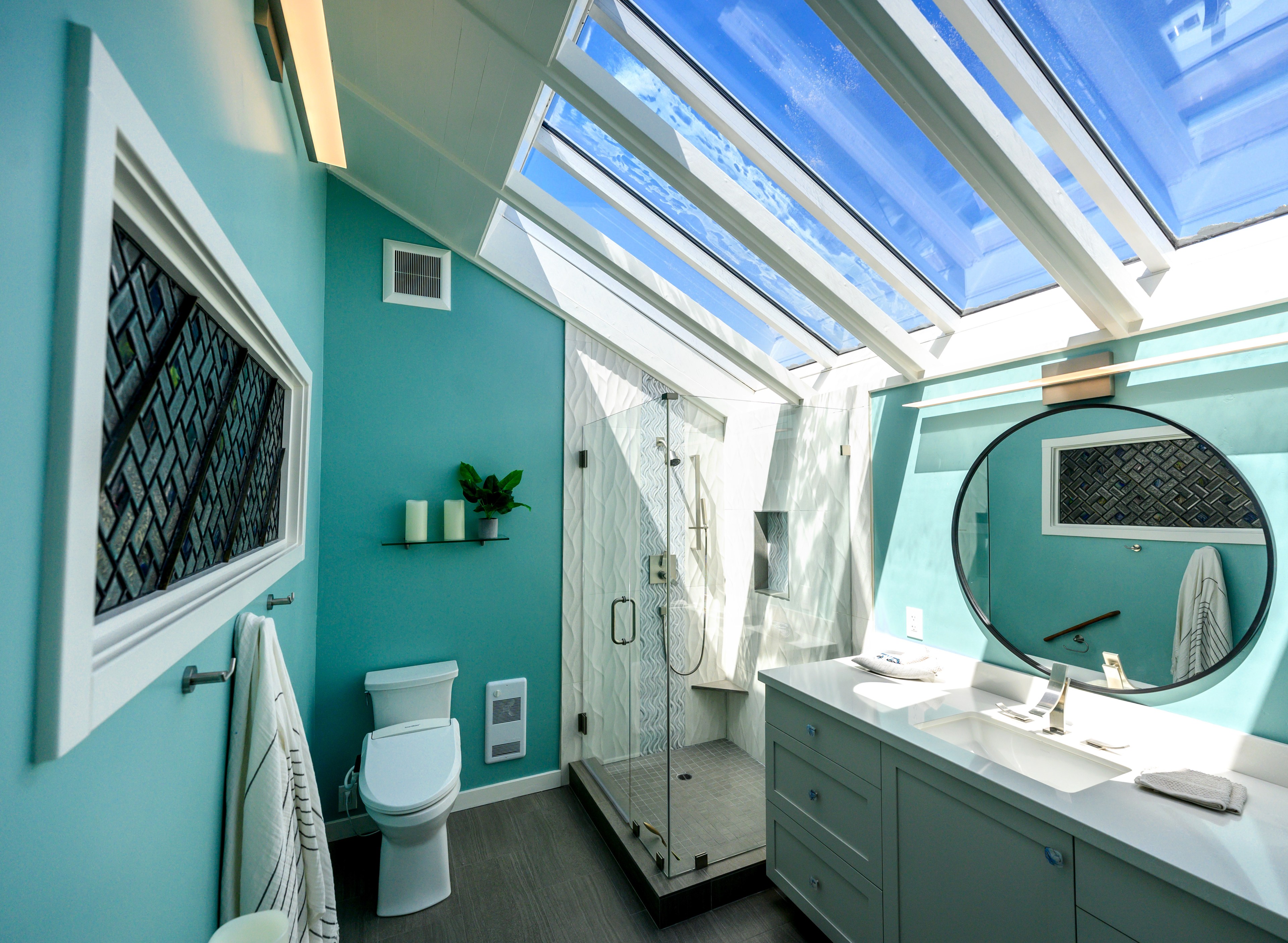 A modern bathroom with a skylight, glass shower, and teal walls.