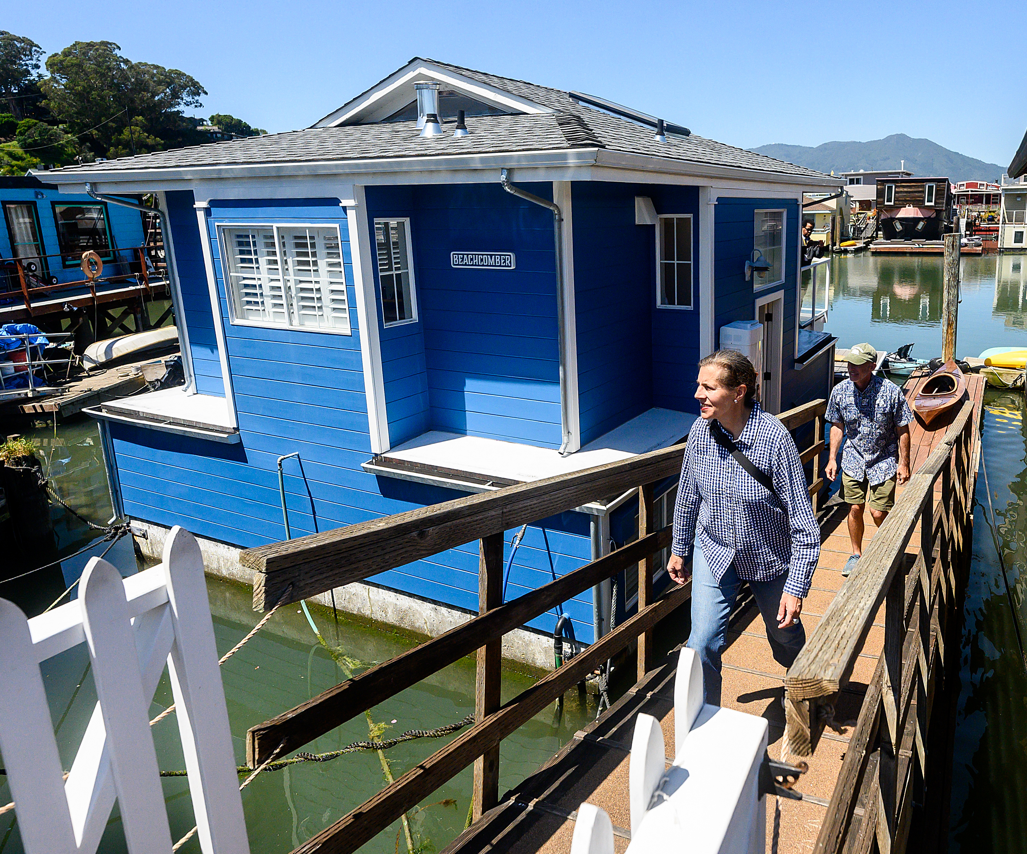 A blue houseboat named &quot;BEACHCOMBER&quot; with people walking on a dock, surrounded by other colorful floating homes.