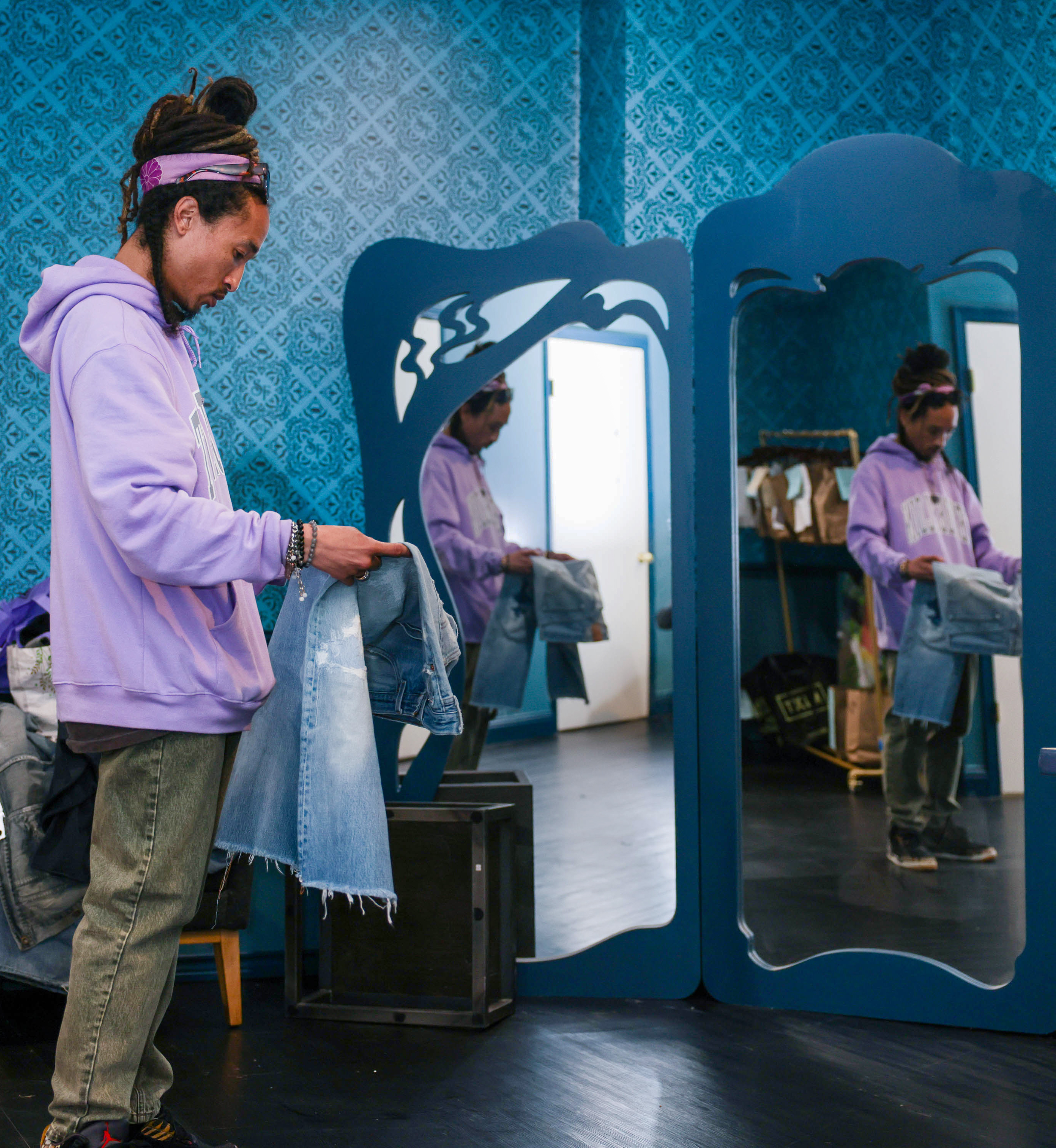 A person in a purple hoodie examines a denim jacket in a dressing room with ornate blue mirrors.