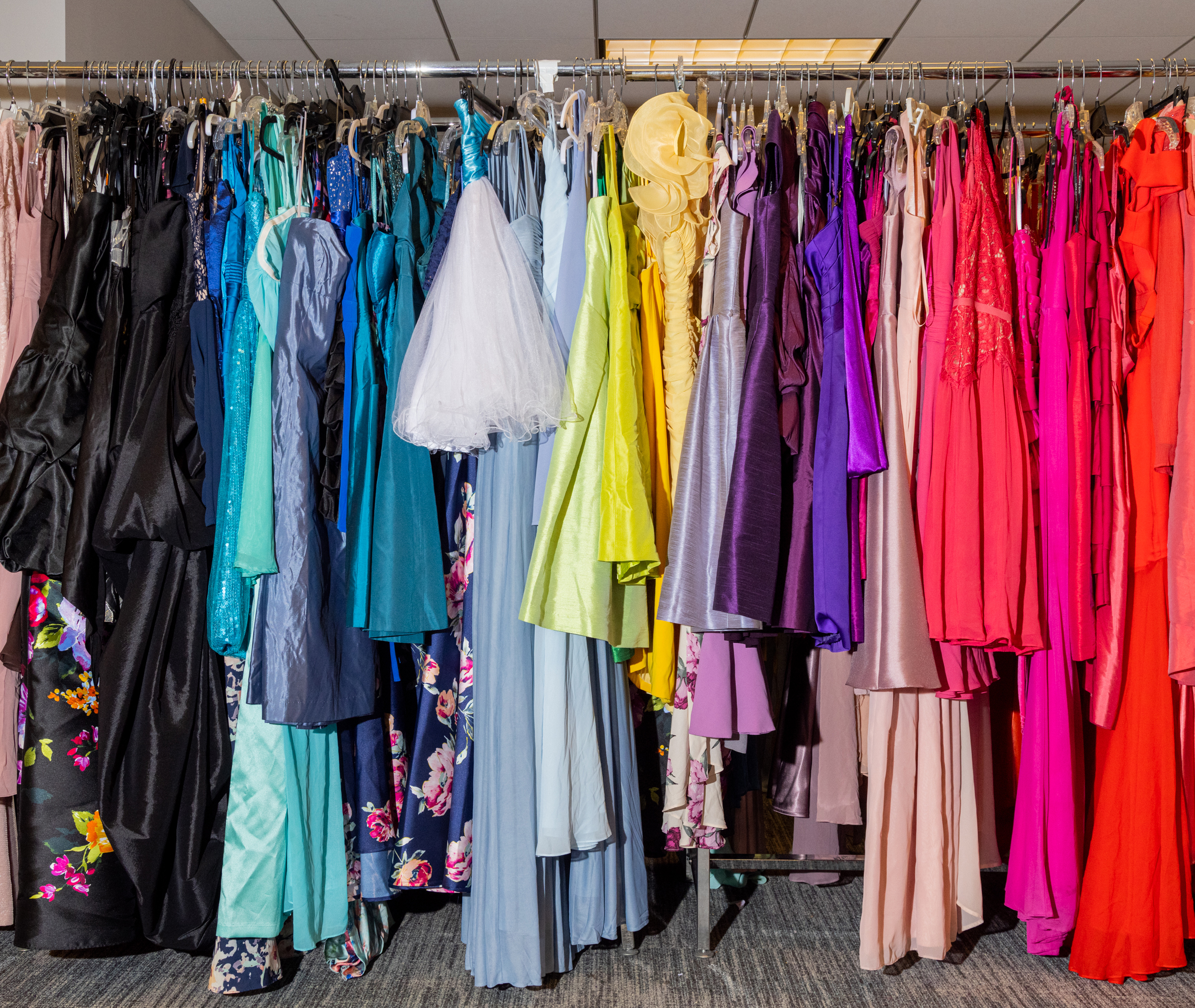 A range of colorful formal dresses hanging on racks in a store.