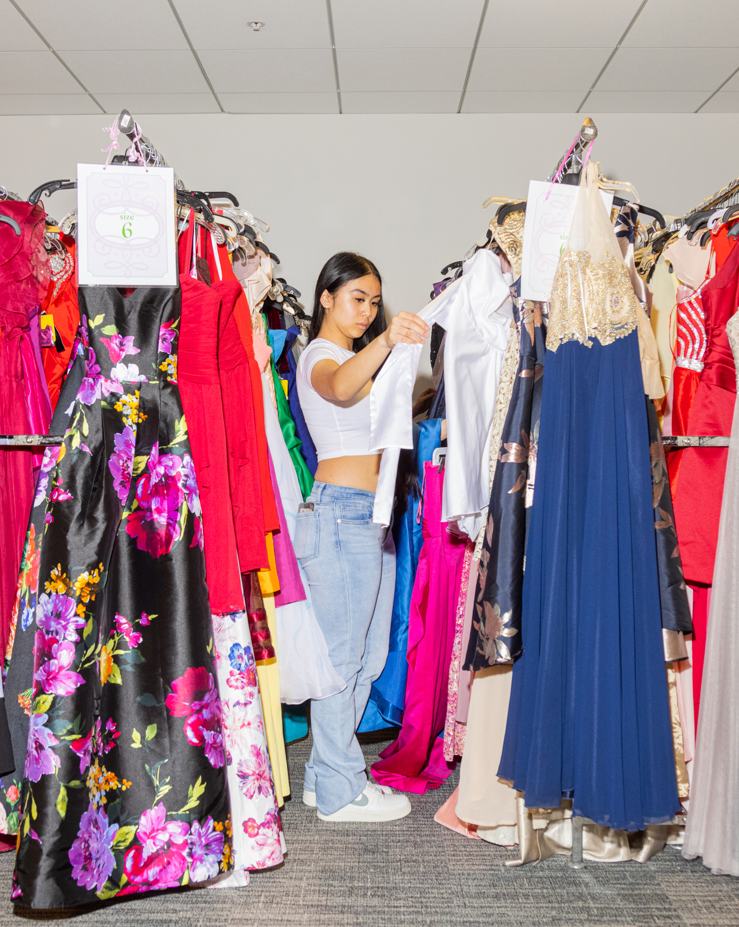 A woman browses through racks of colorful dresses, holding a white garment.