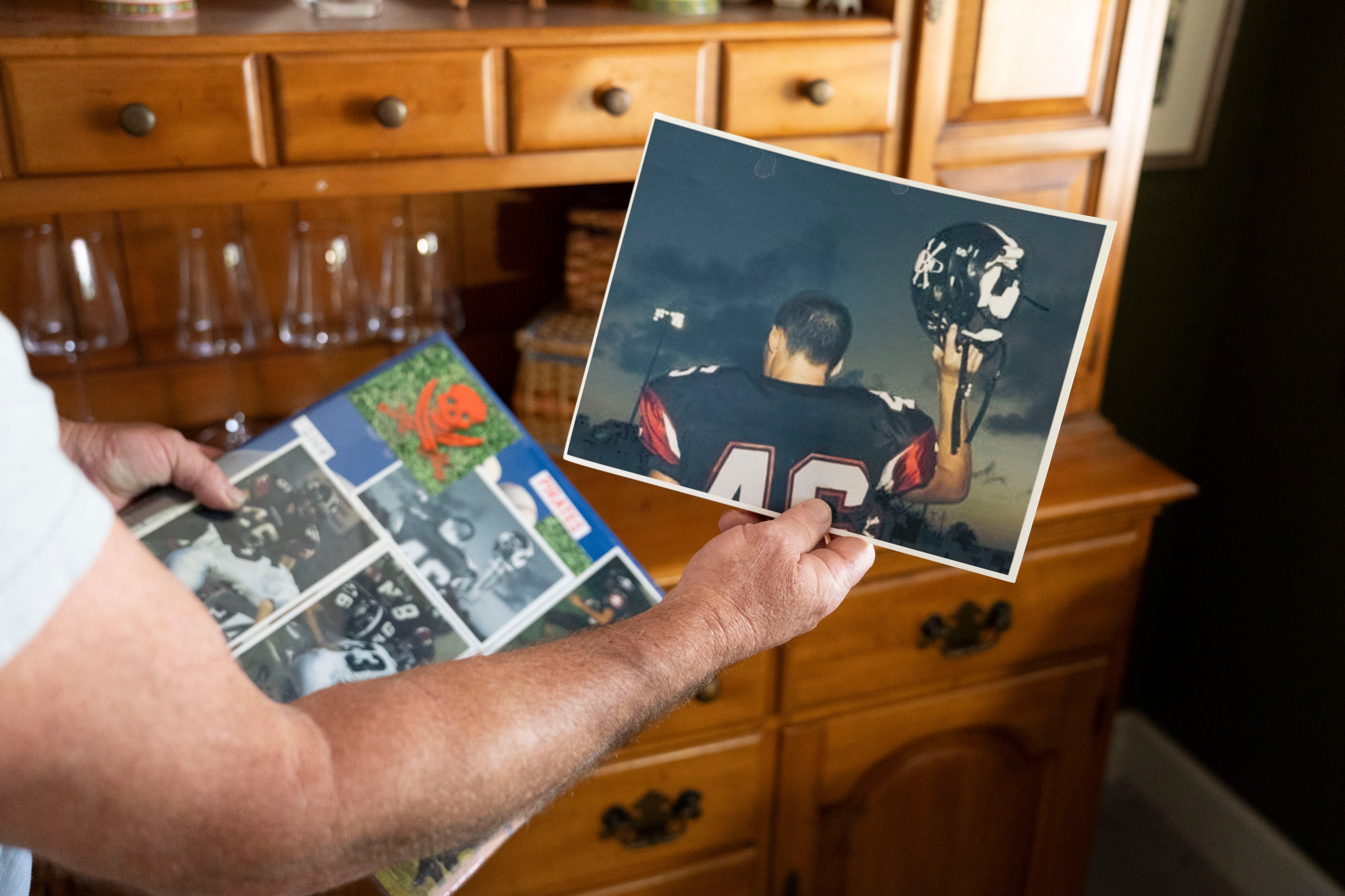 A person holds a photo of a football player (#46) and a scrapbook with sports images on a wooden table.