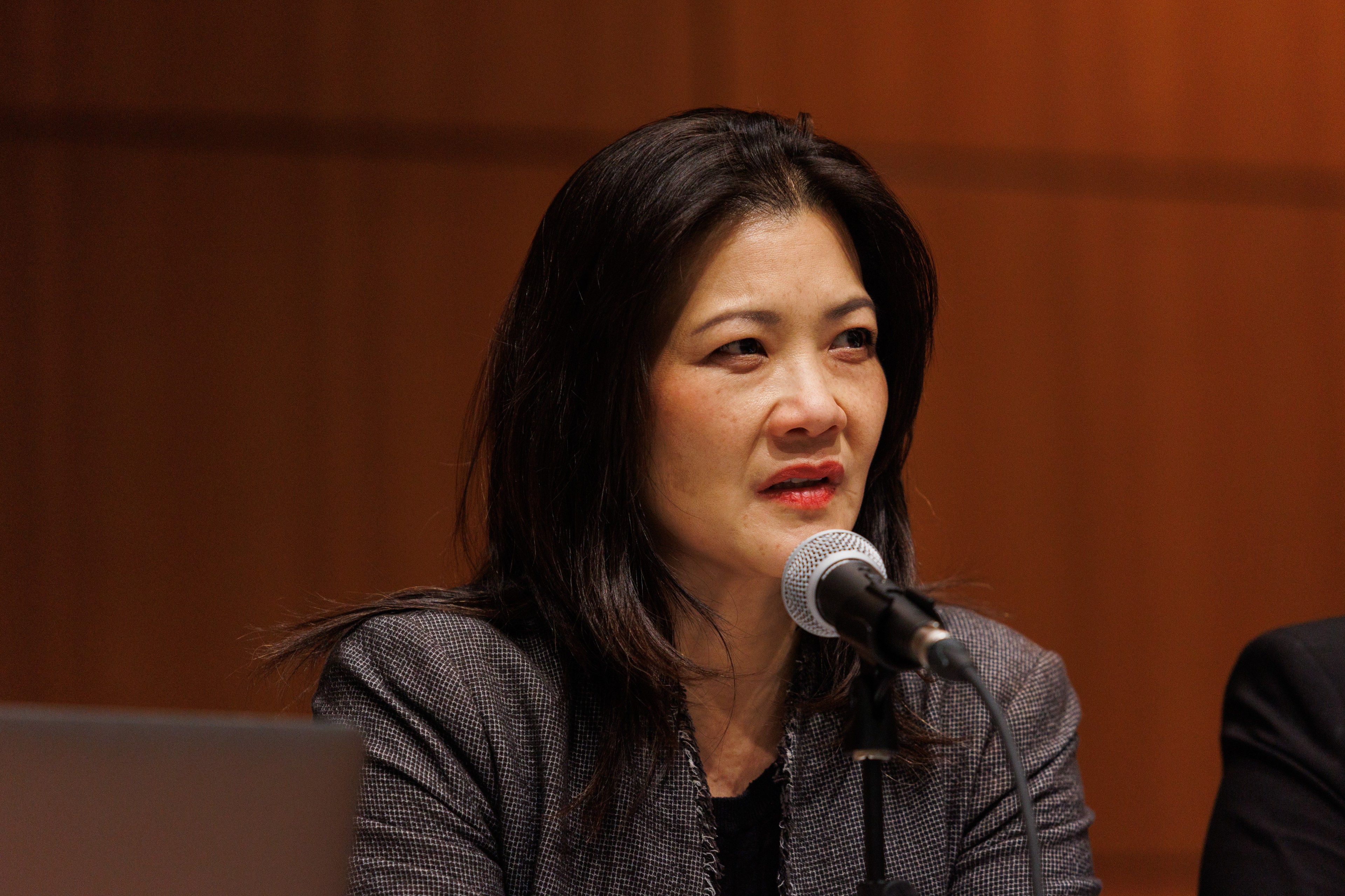 Nancy Tung speaks into a microphone. She looks focused, has long dark hair and wears a tweed blazer.
