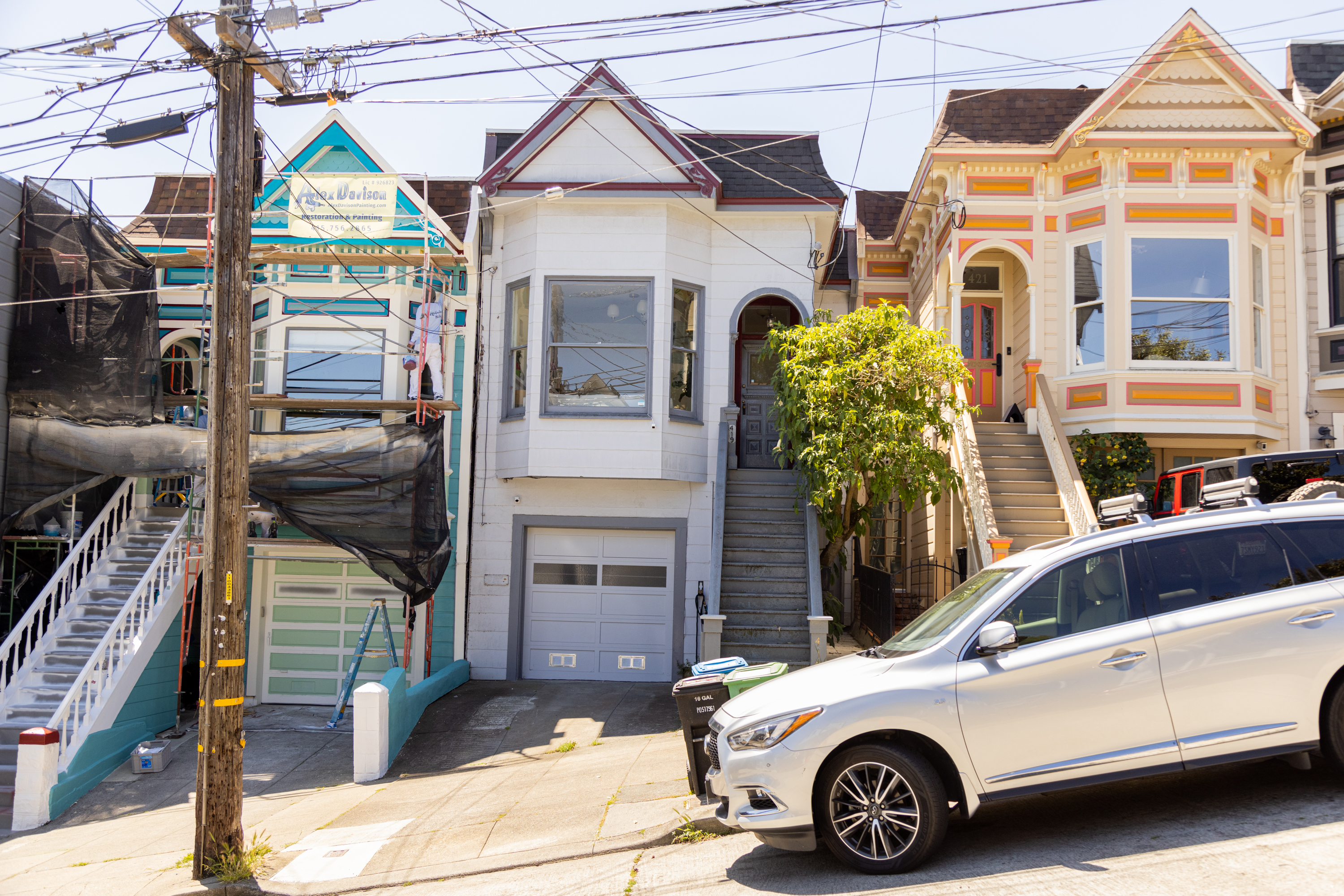 Victorian houses on a sunny, steep street with a parked car in the foreground.