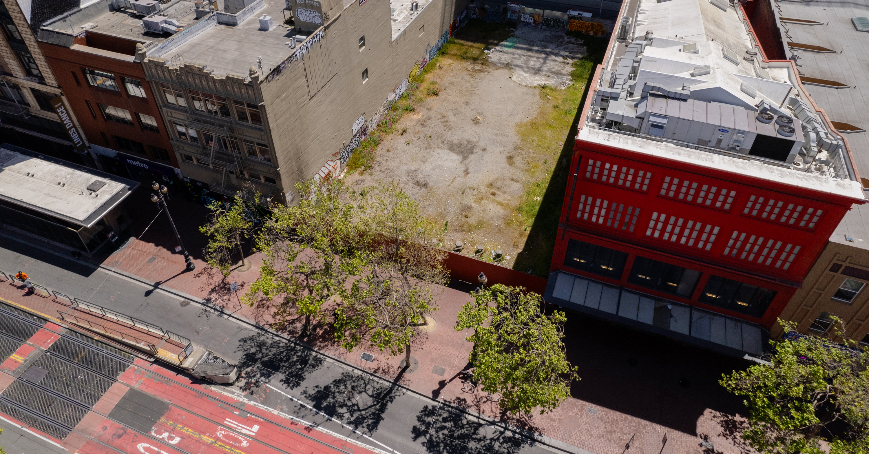 An aerial view of an empty lot with two multistory buildings next to it.