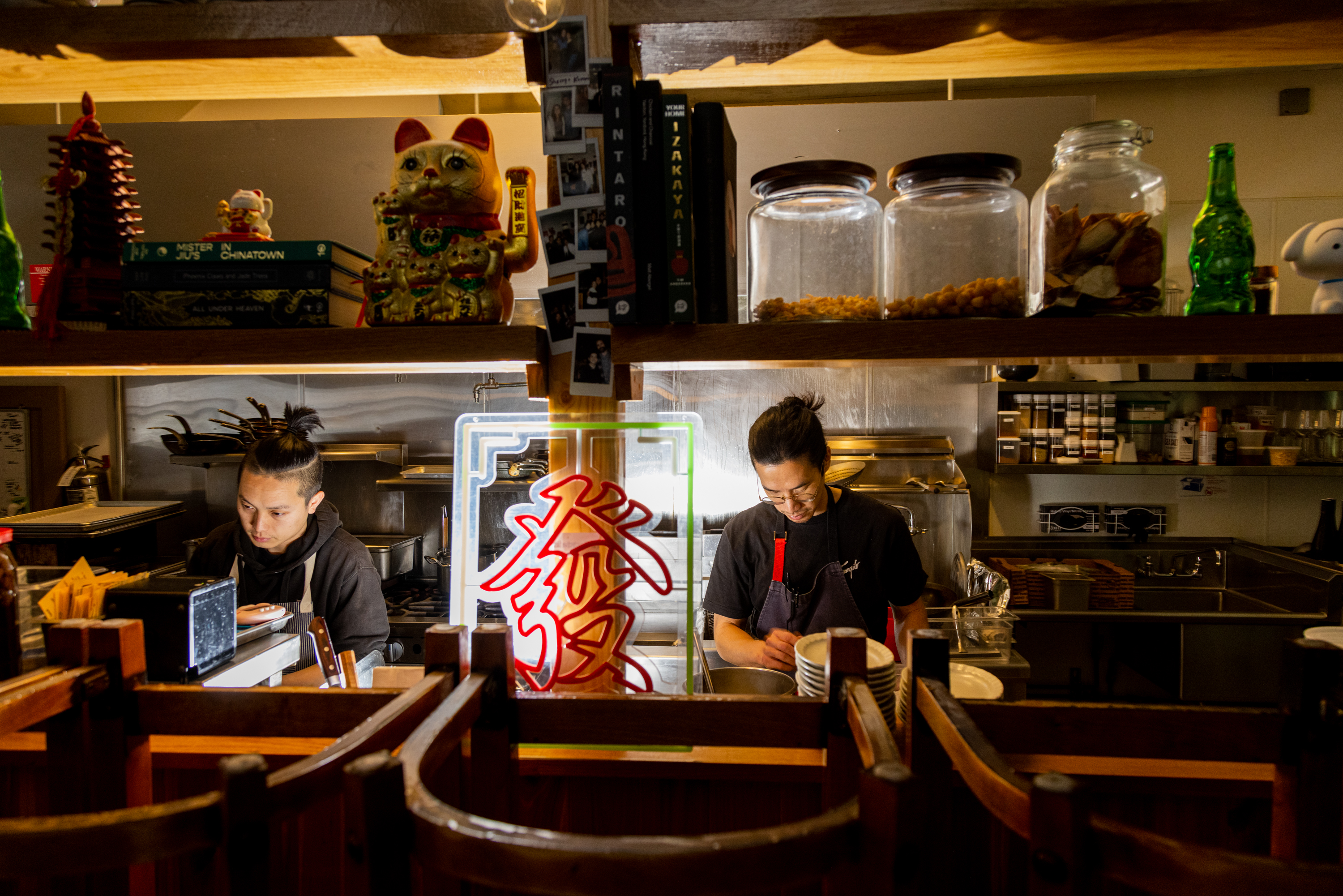 Two people working in a cozy, dimly lit Asian restaurant with cultural decorations and a neon sign.