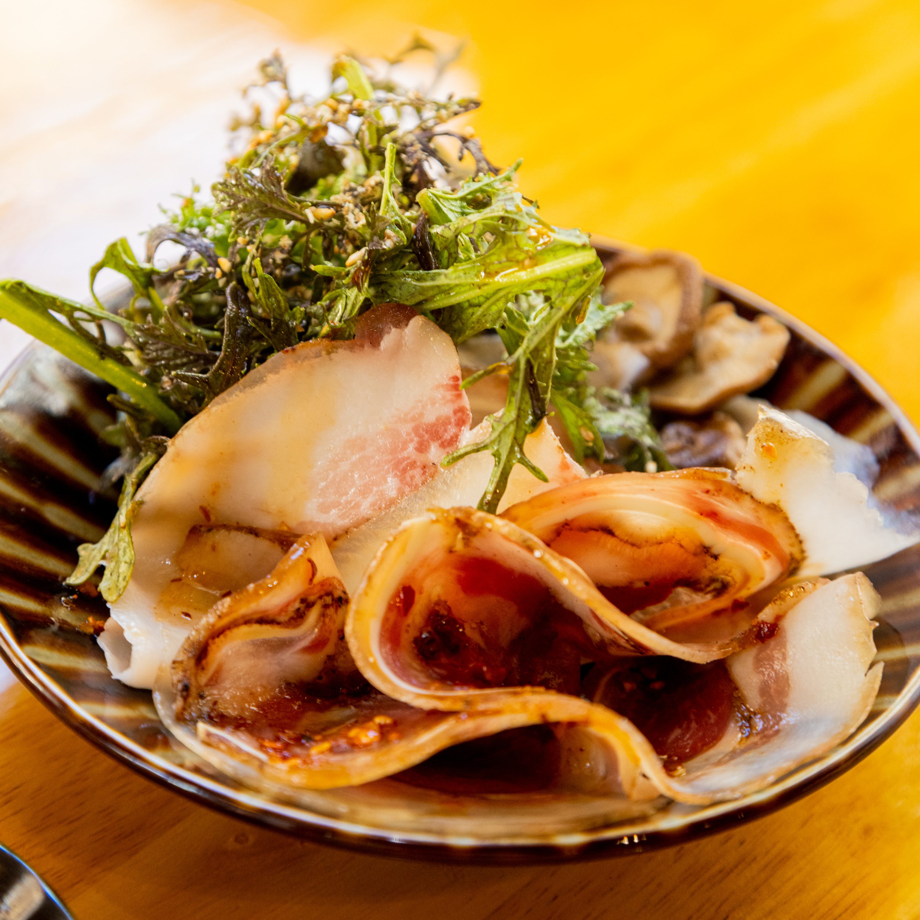 A dish with sliced seafood and green herbs on a brown-striped plate, with vibrant colors on a yellow table.