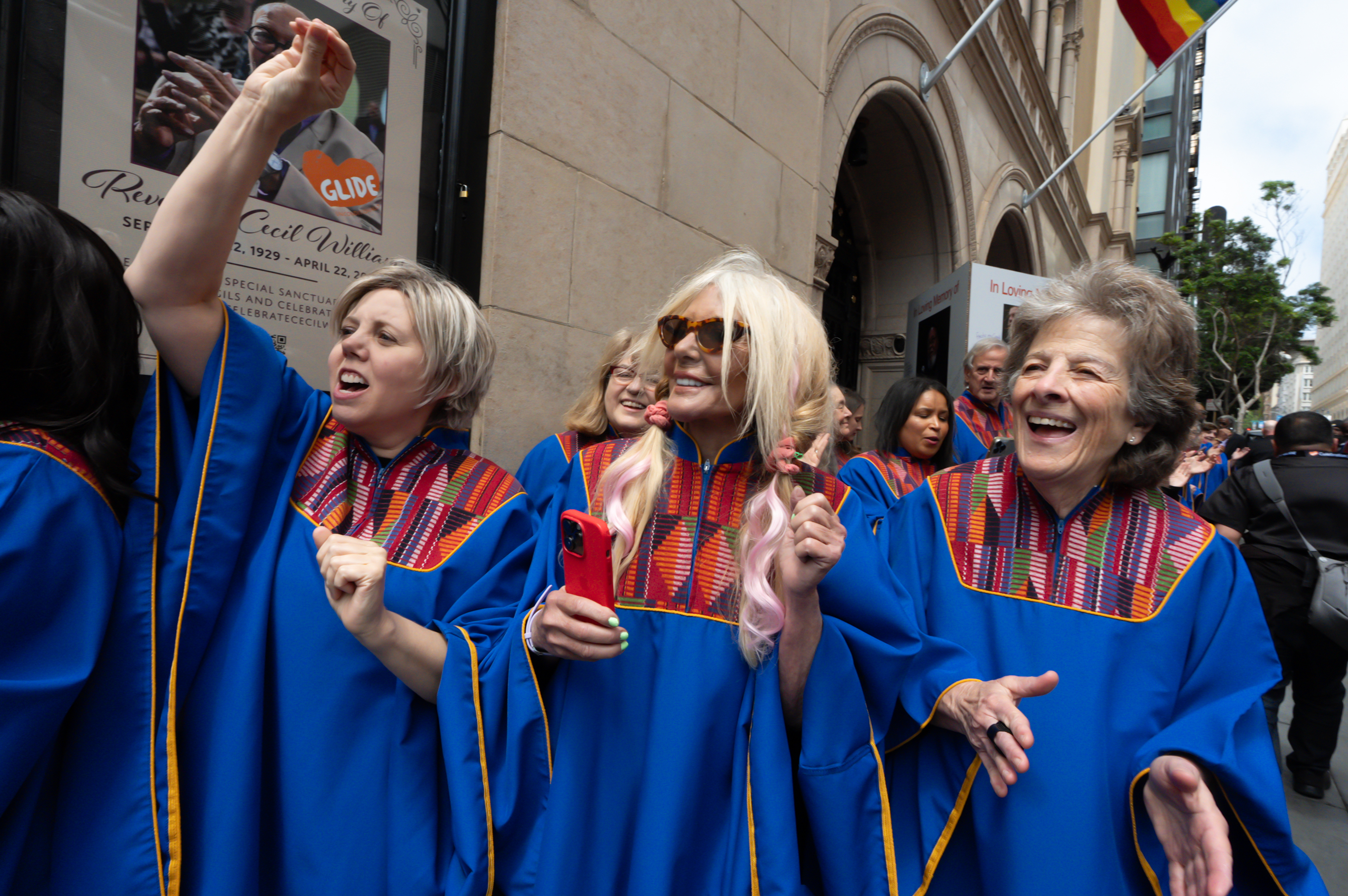 Joyful people in blue robes with colorful stoles are walking and celebrating outside.