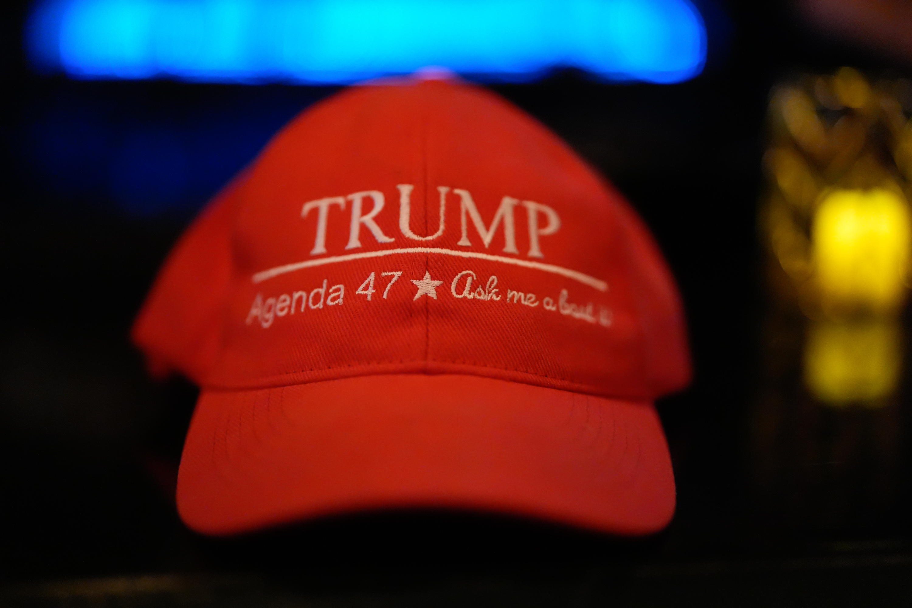 The image shows a red baseball cap with &quot;TRUMP&quot; in white letters, followed by &quot;Agenda 47 * Ask me about it&quot; embroidered underneath.