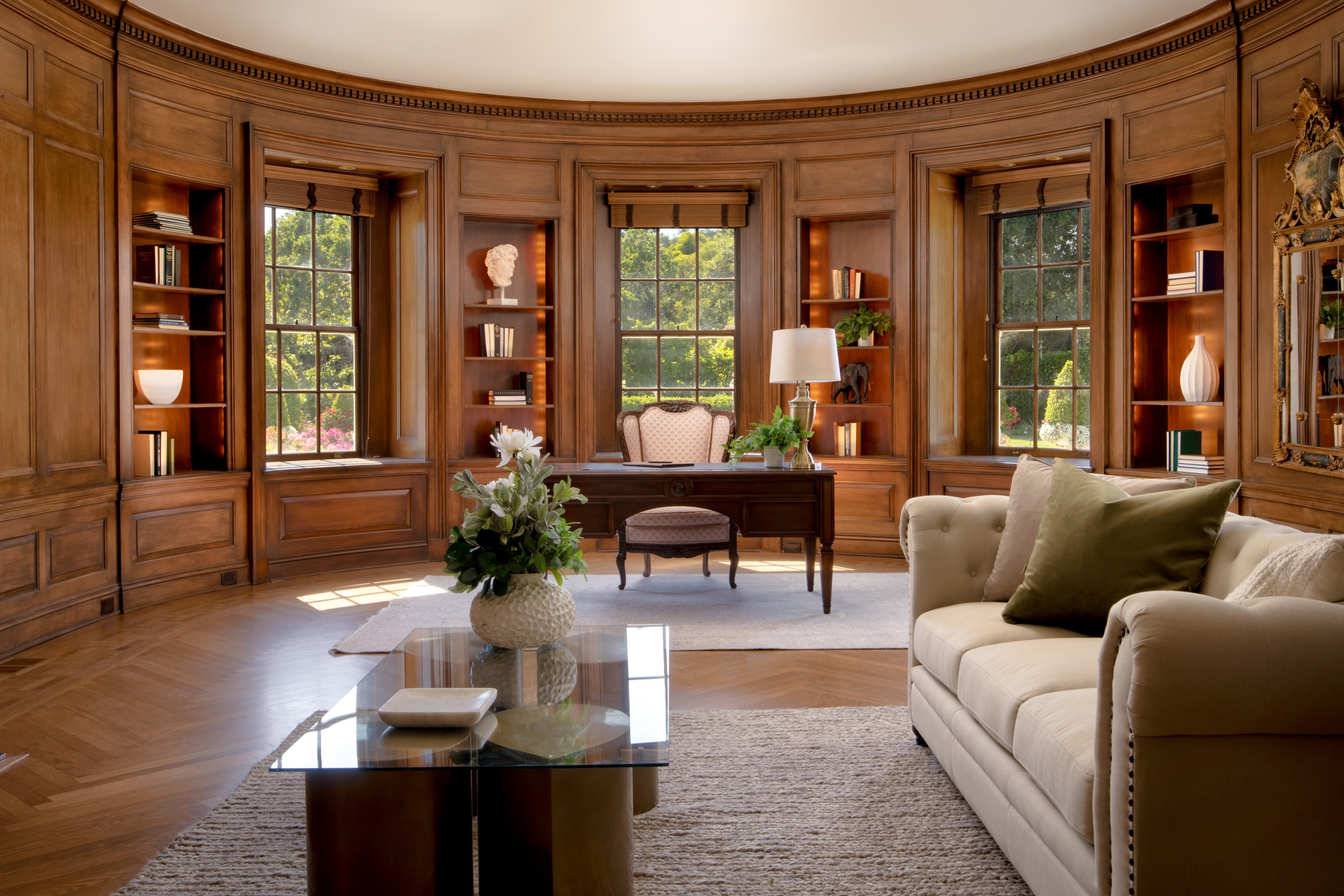 An estate room with a wood-lined, window-ringed interior looks out on a sunny tree-lined yard