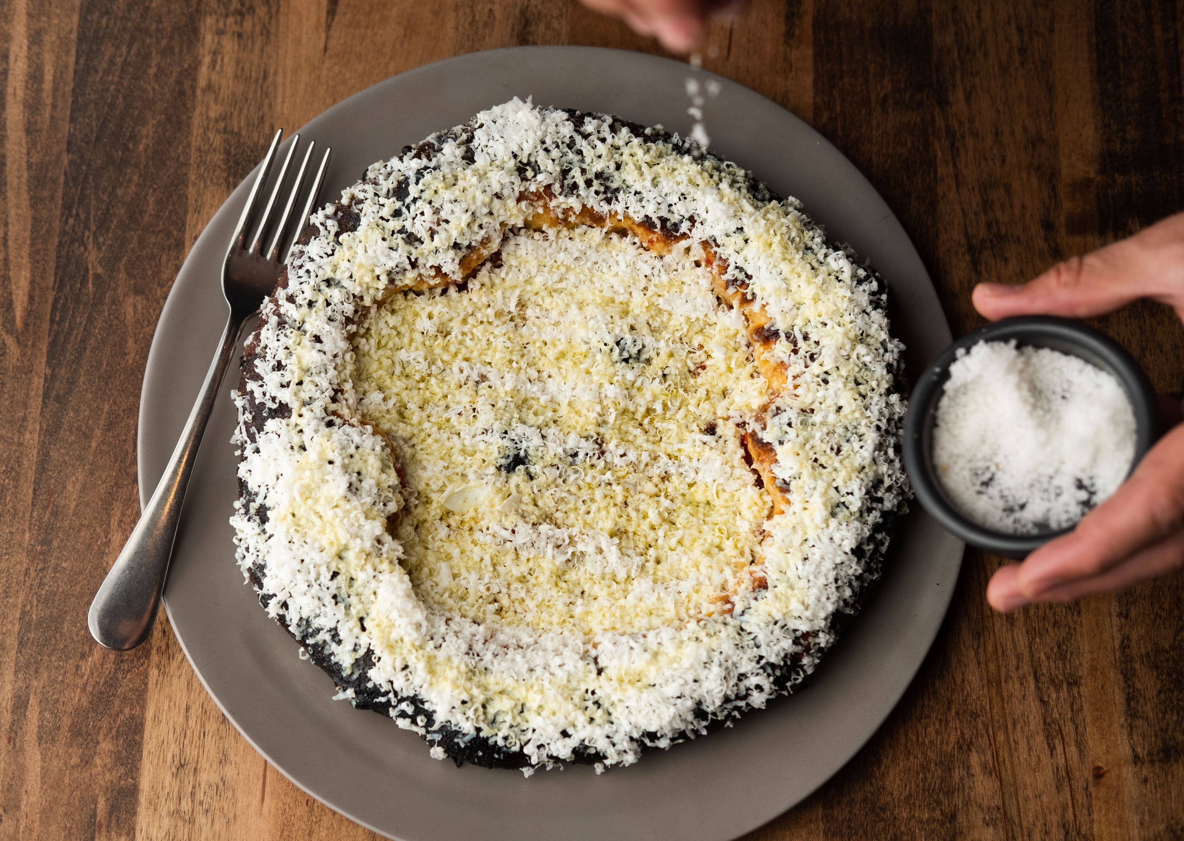 A circular white ricotta cheese pizza on a gray plate with a person sprinkling salt from above.