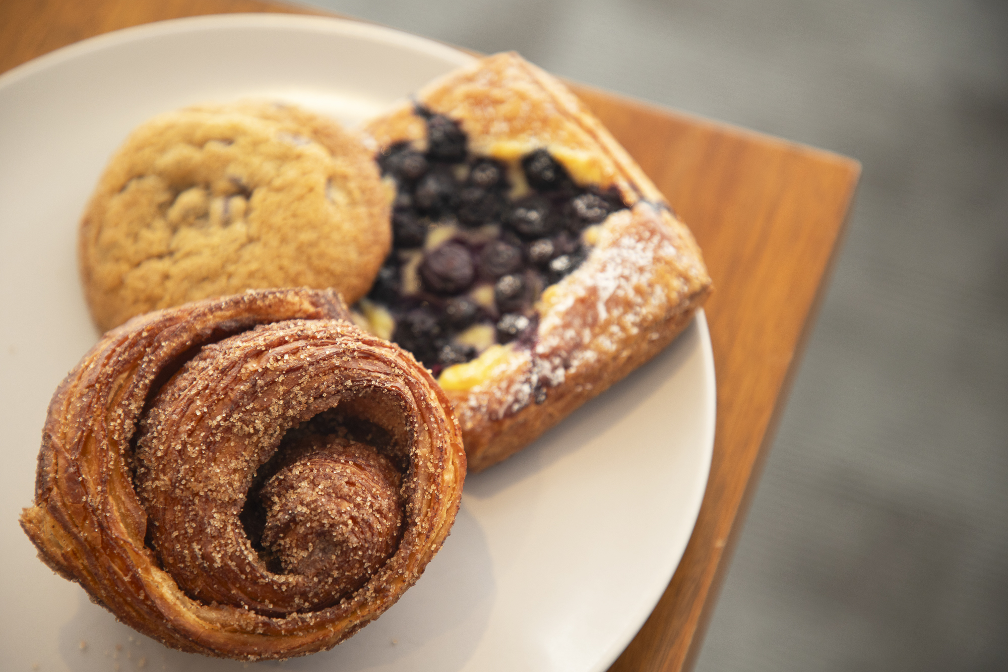 A morning bun, chocolate chip cookie and blueberry and cheese danish sit on a gray plate.