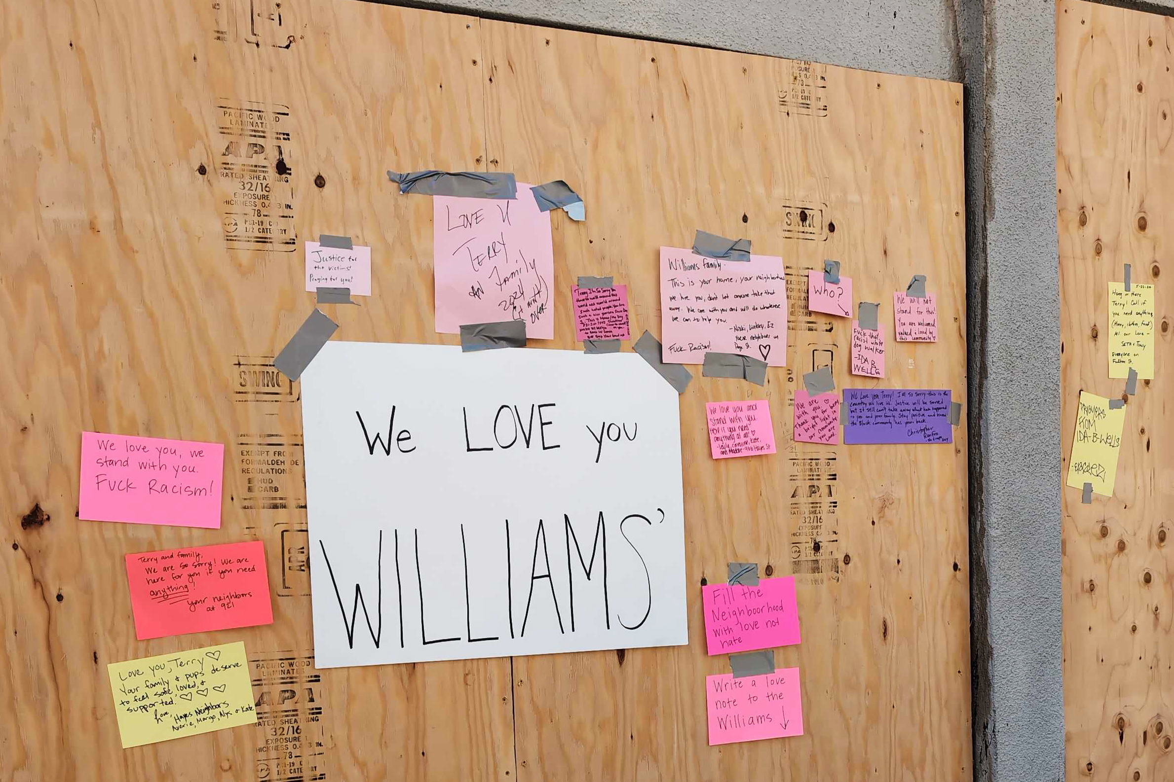A plywood wall covered with various handwritten notes of support taped on. A large central sign reads, "We LOVE you WILLIAMS'."