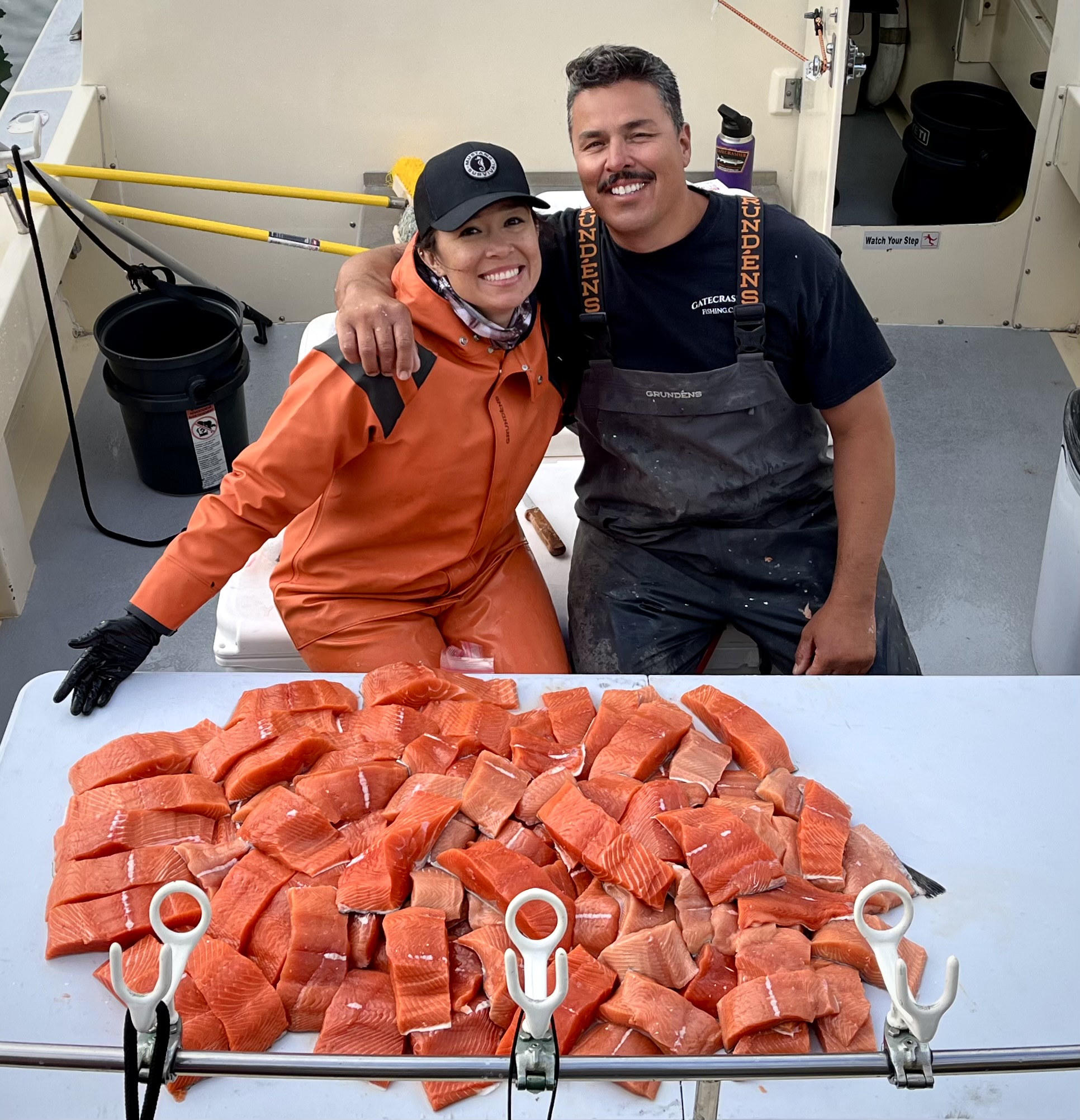 Two boat captains pose for a photo on a boat beside salmon filets.