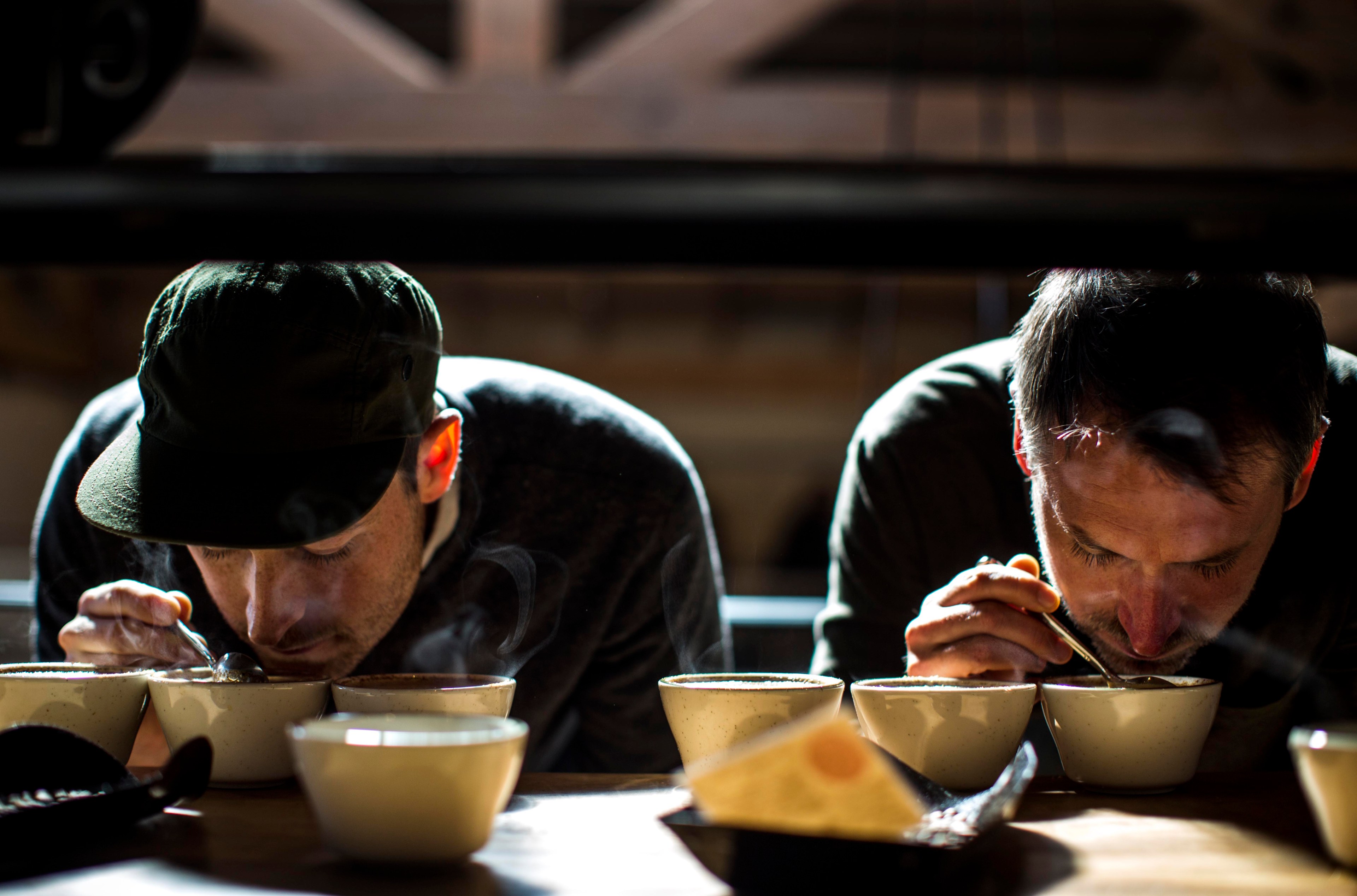 Two men (Justin and Jerad Morrison, the founders of Sightglass Coffee) lean over cups of coffee.