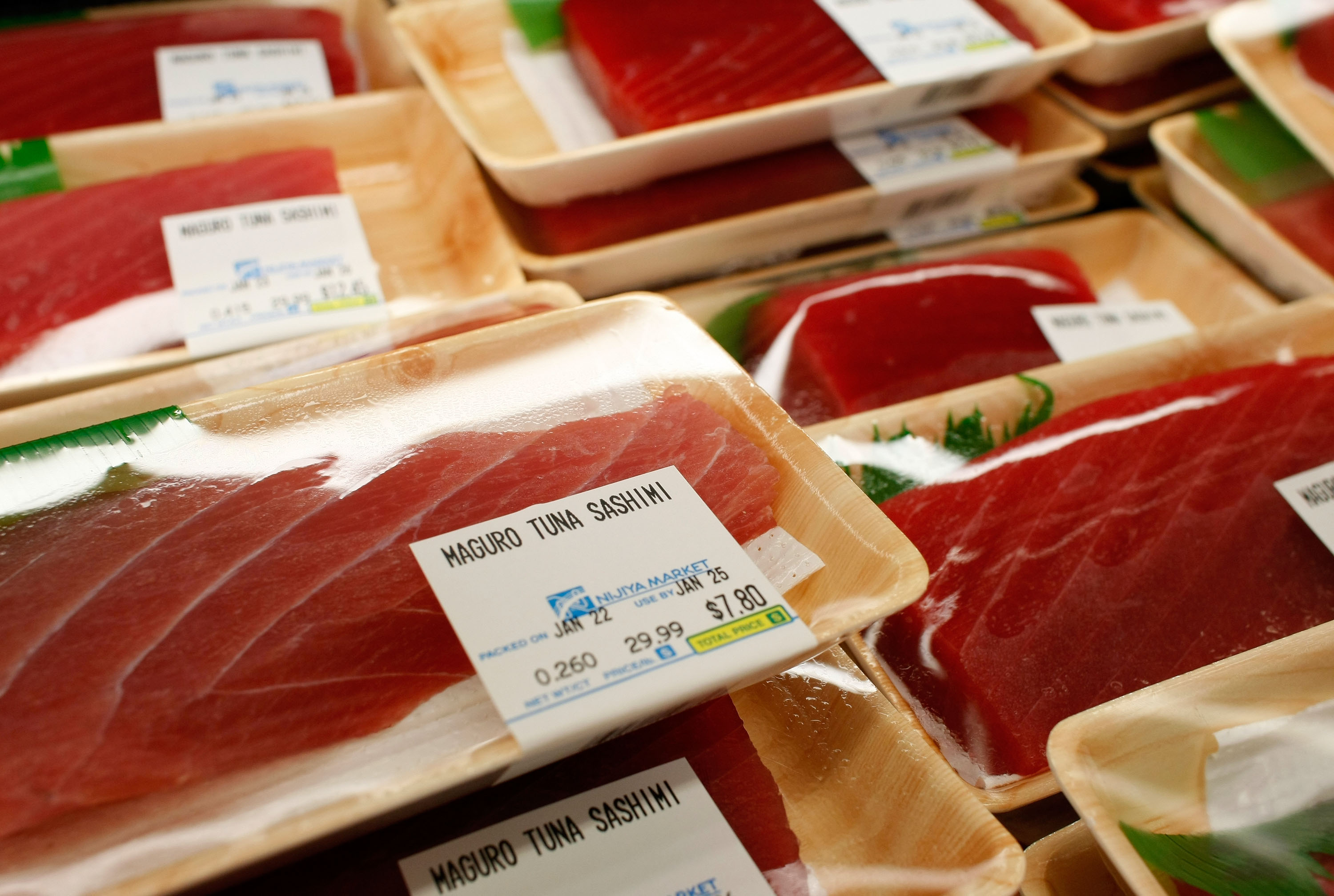 Packages of maguro tuna sashimi are displayed in plastic-wrapped trays with price and weight labels, showcasing the deep red cut of fish.