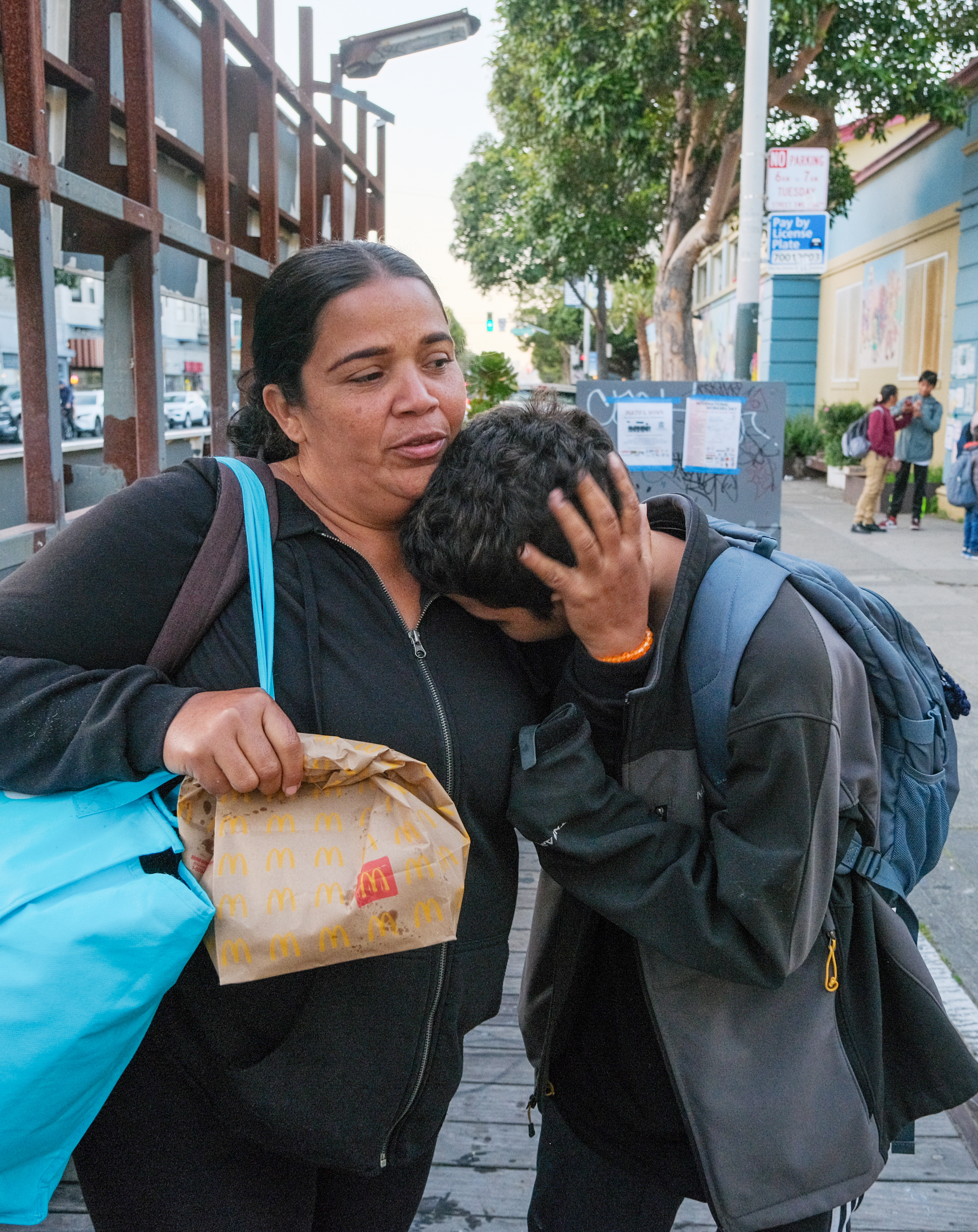 A woman holding a McDonald's bag embraces a distressed child on a city sidewalk.