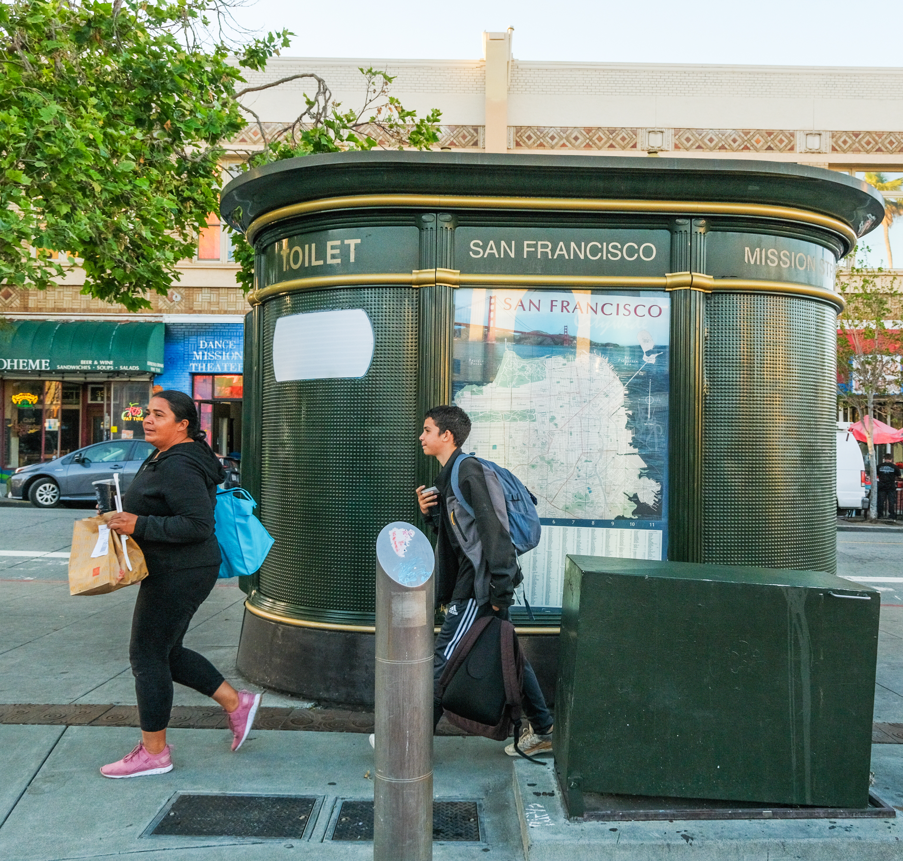 A self-cleaning public toilet in San Francisco with people walking by on the sidewalk.