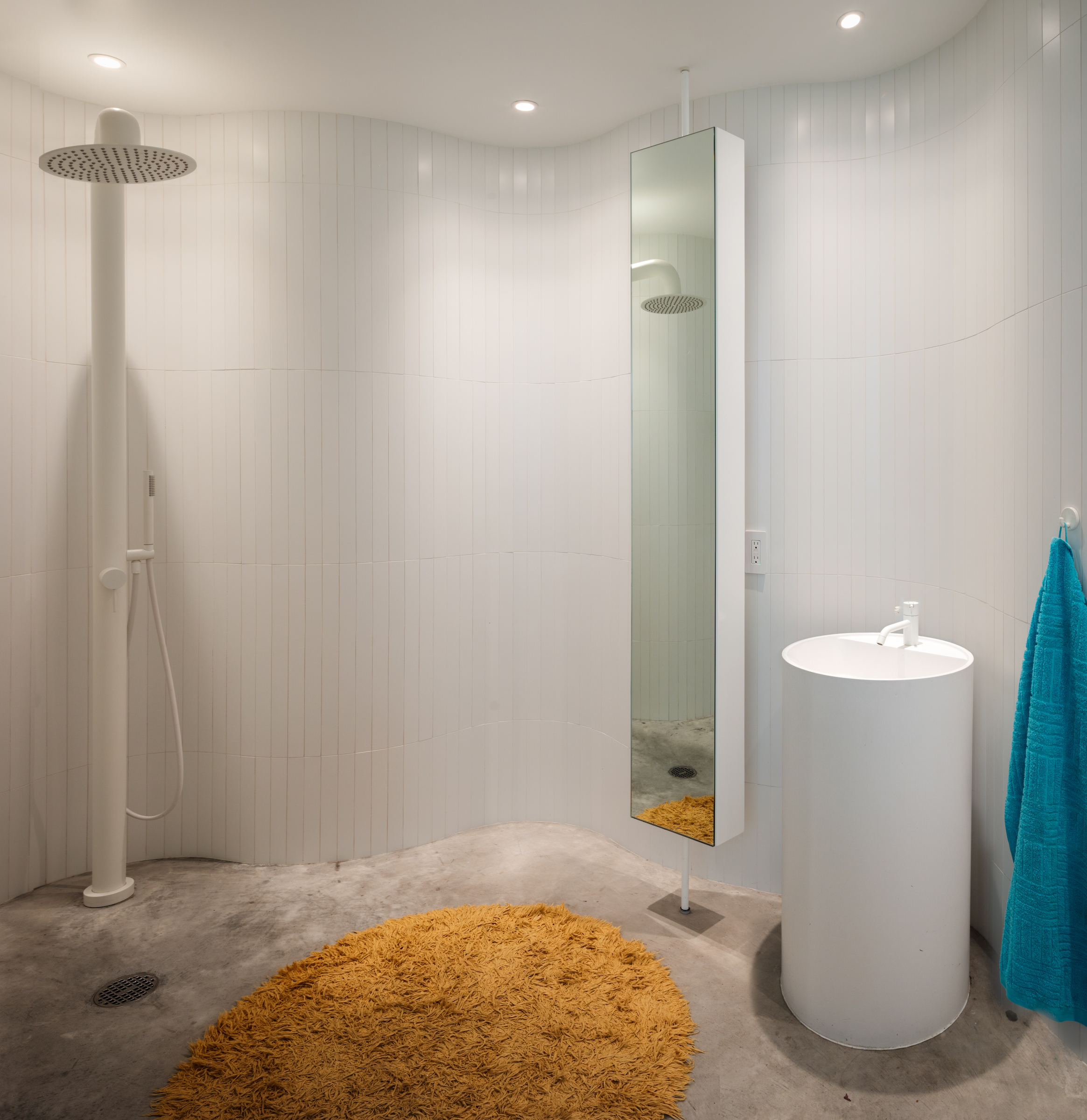 Modern bathroom with a white cylindrical sink, a shaggy orange rug, and a glass shower enclosure with a rain showerhead.