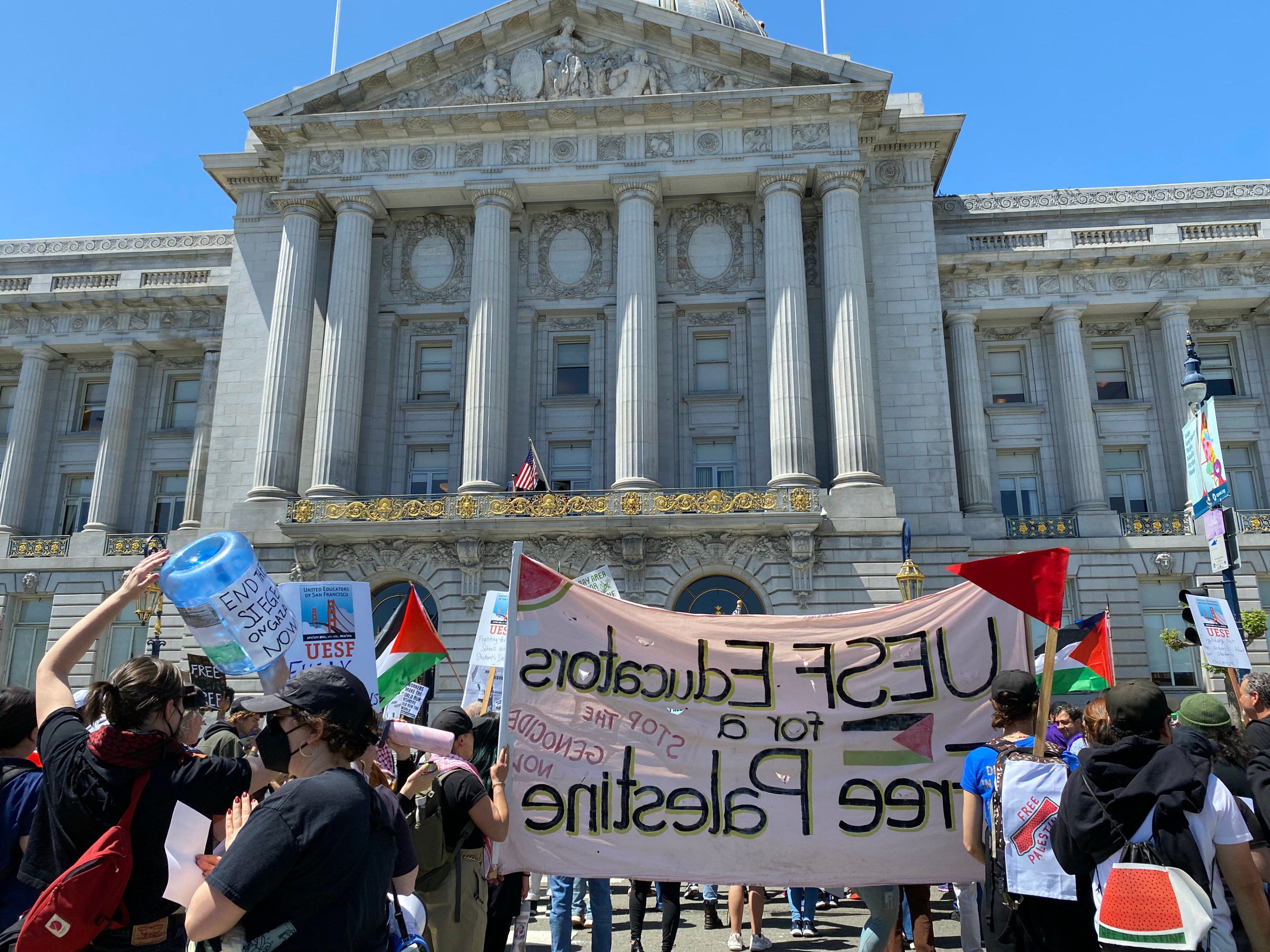 Protesters with banners in front of a grand building on a sunny day.