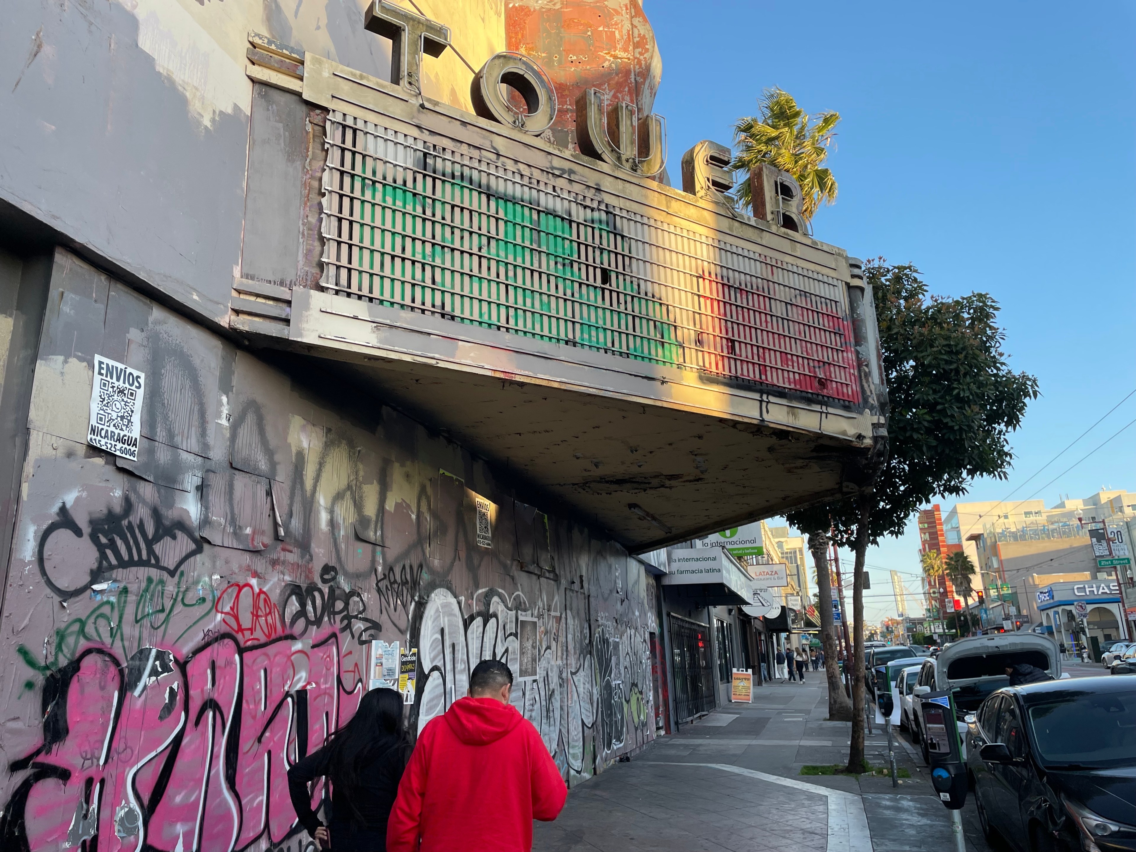 People walk in front of a ruined movie theater.