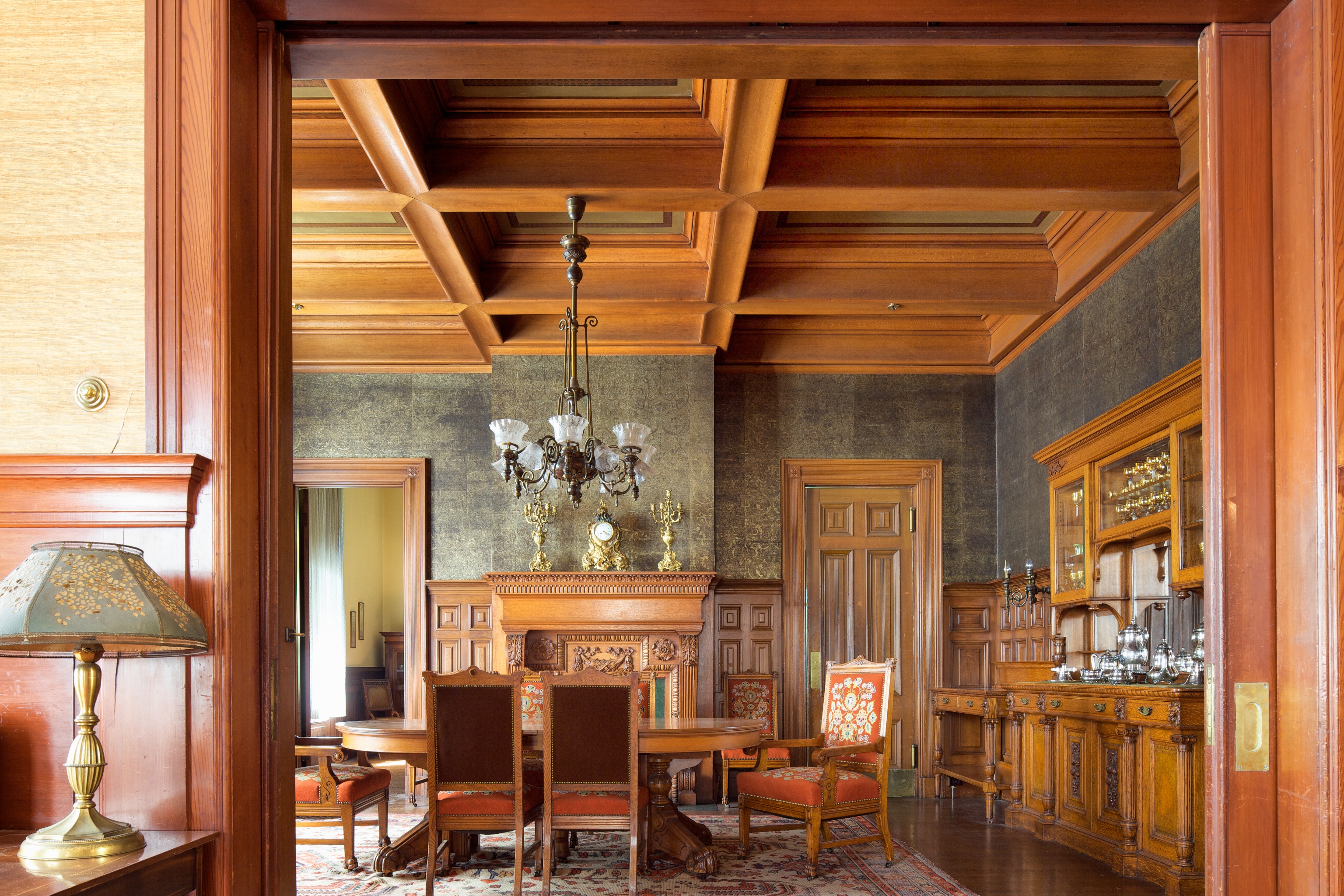 An elegant room with wood-paneled walls, coffered ceiling, antique furniture, and a chandelier.