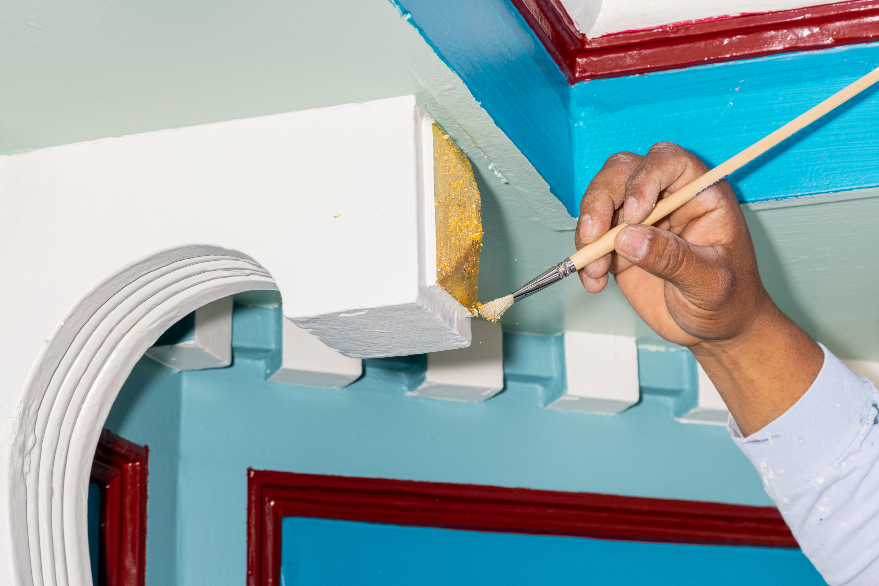 A hand is painting the edge of vibrant, multicolored architectural features.