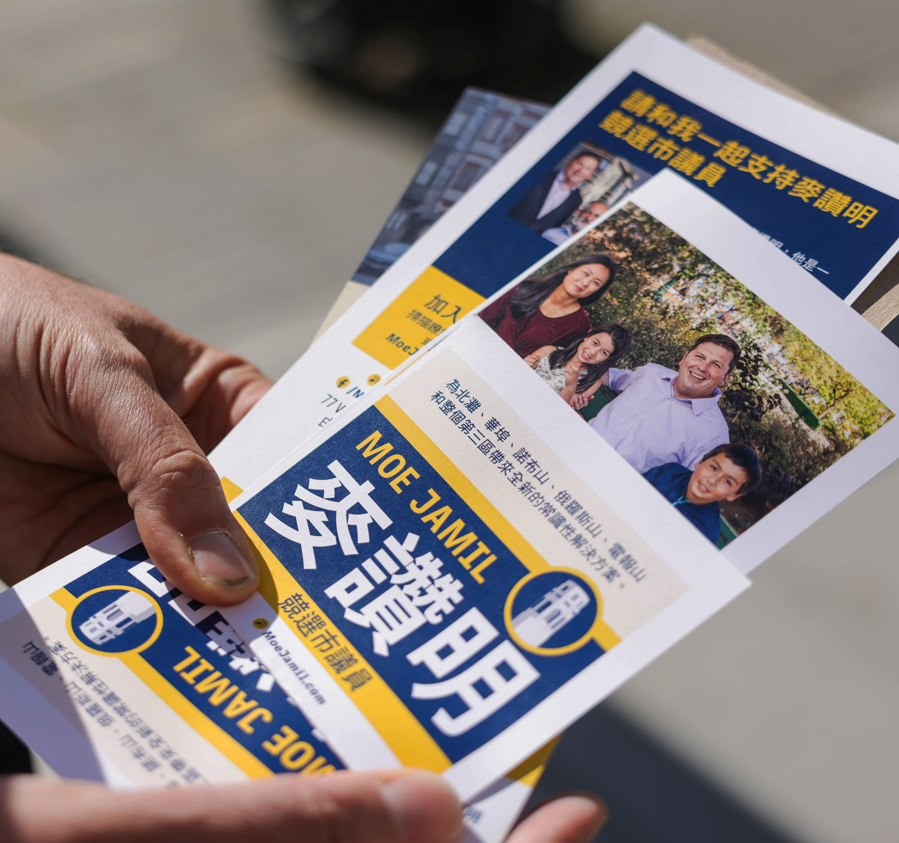 A hand holds a flyer with Chinese text, photos of smiling people, and blue-yellow design elements.