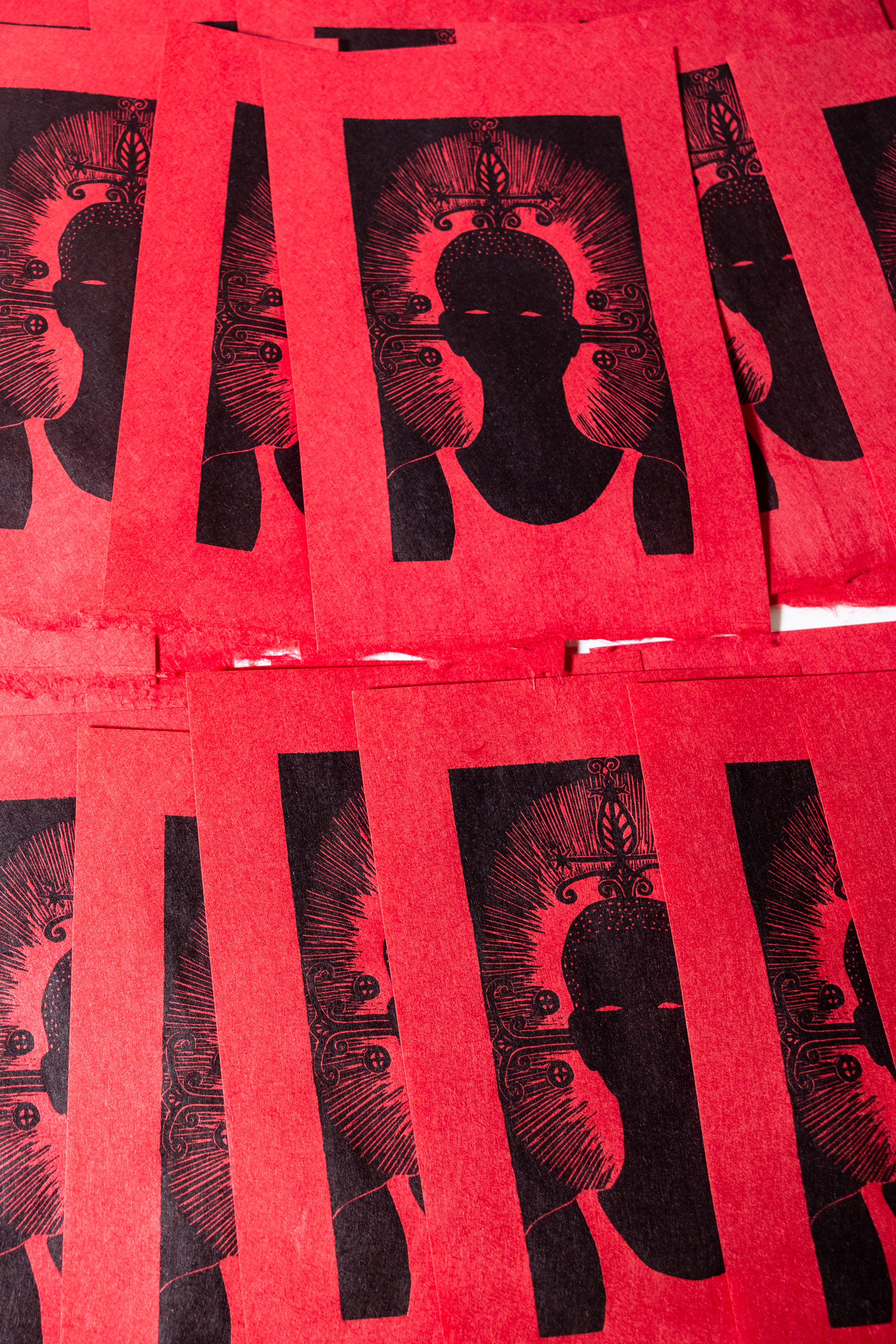 Red Chinese paper with black printed designs of a traditional Buddha face surrounded by intricate patterns. Multiple overlapping sheets visible.