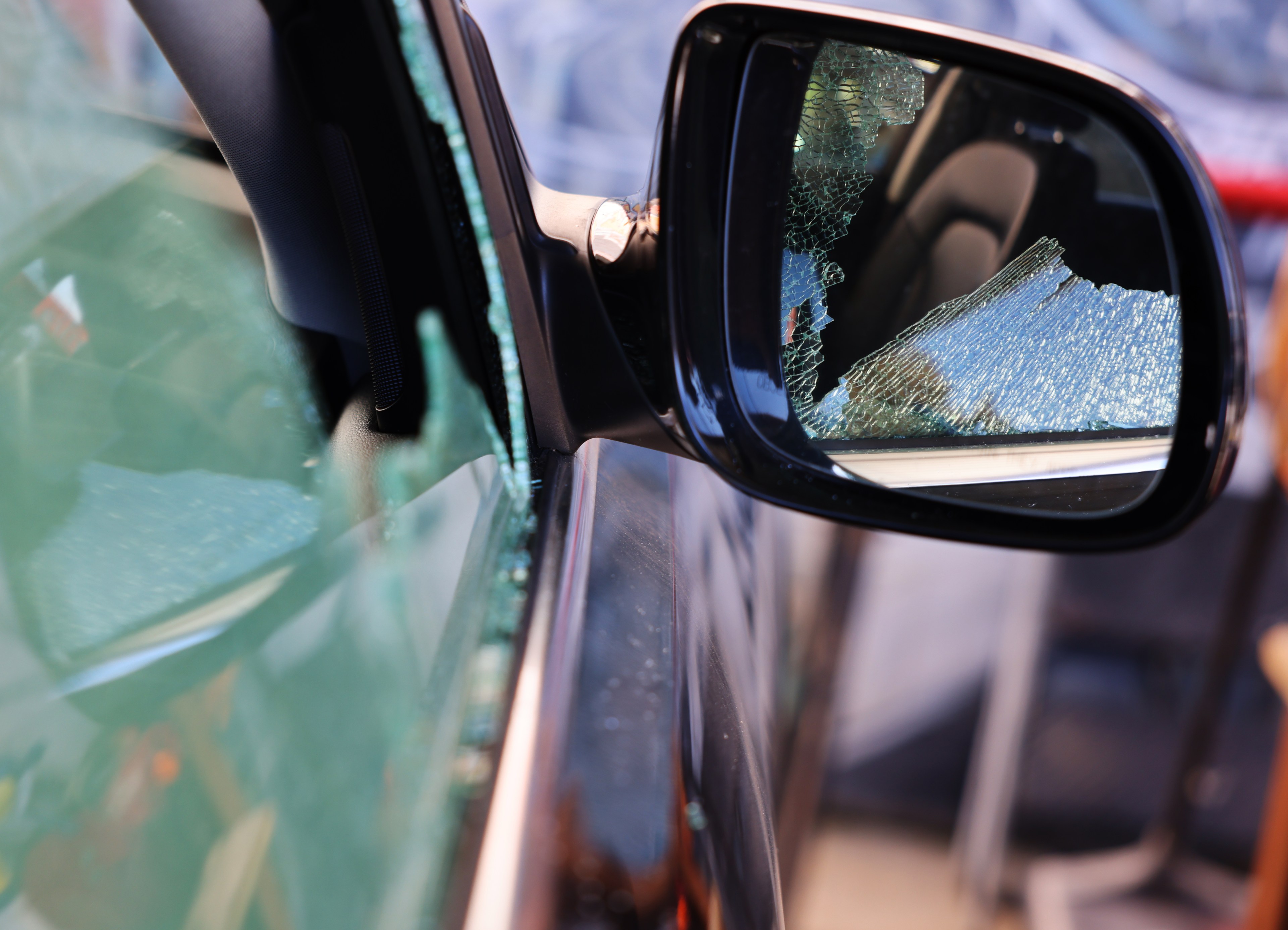 The image shows the exterior side mirror of a car, reflecting shattered glass from a broken window. The broken glass is visible around the mirror and inside the car.