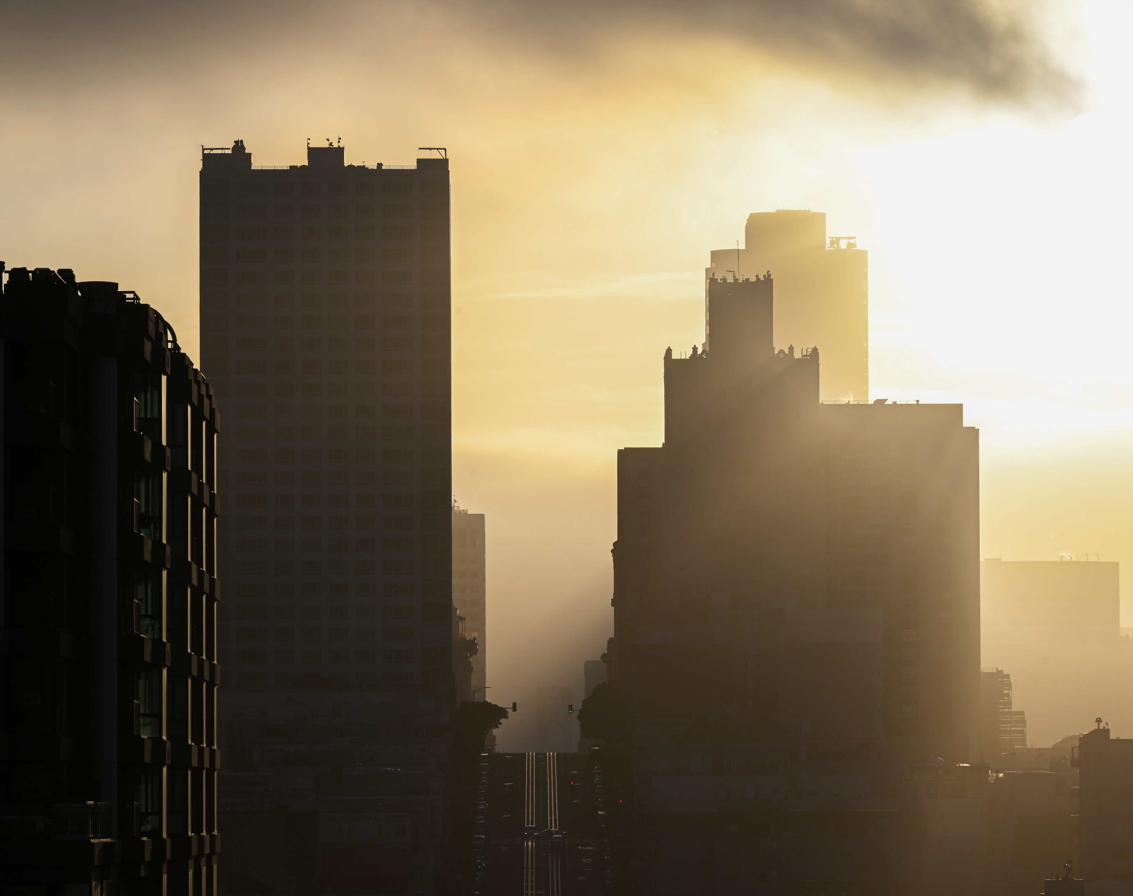 The image shows a cityscape at sunrise, with silhouette skyscrapers bathed in golden light and hazy clouds.