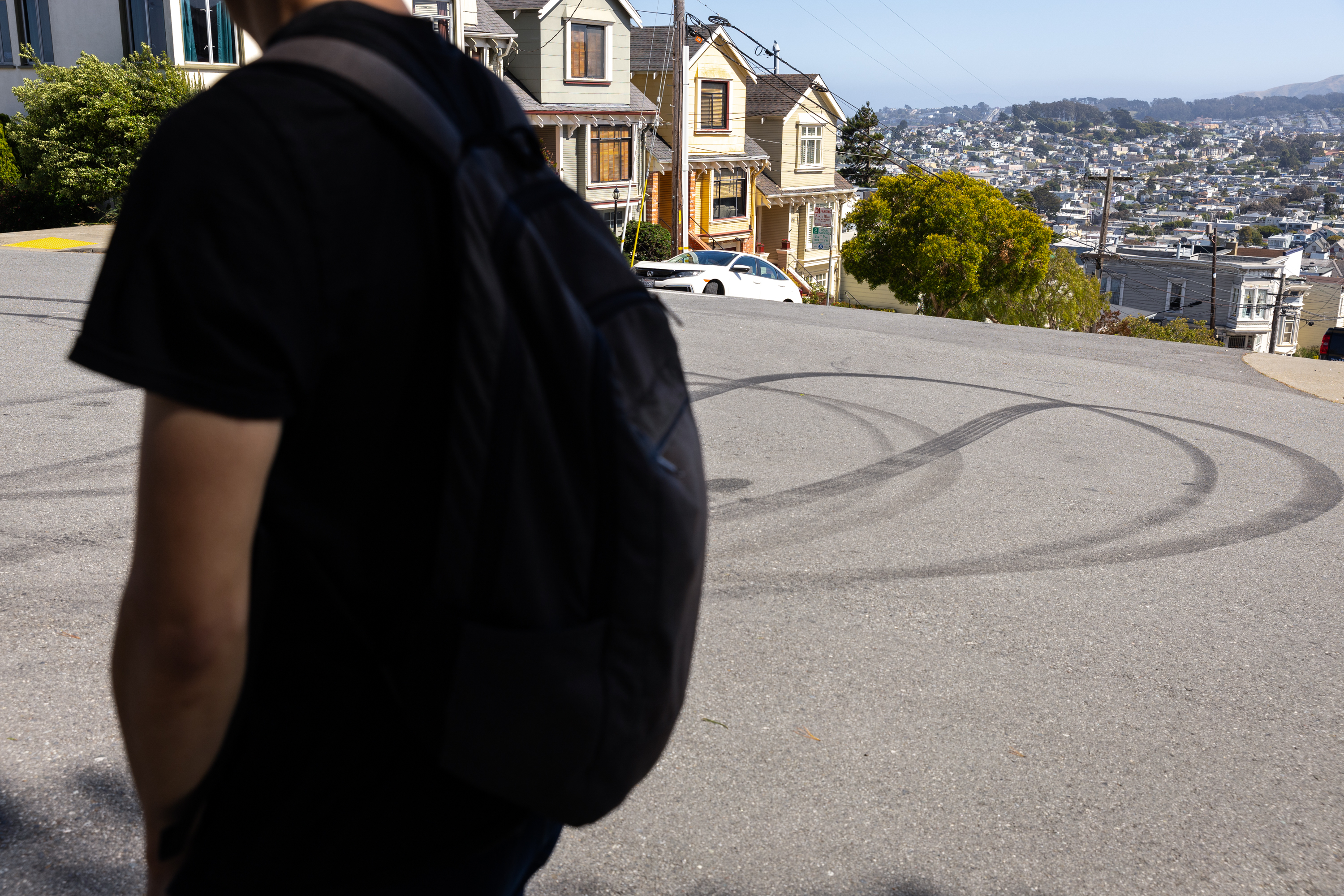 A man wearing a backpack walks next to a street with skid marks.