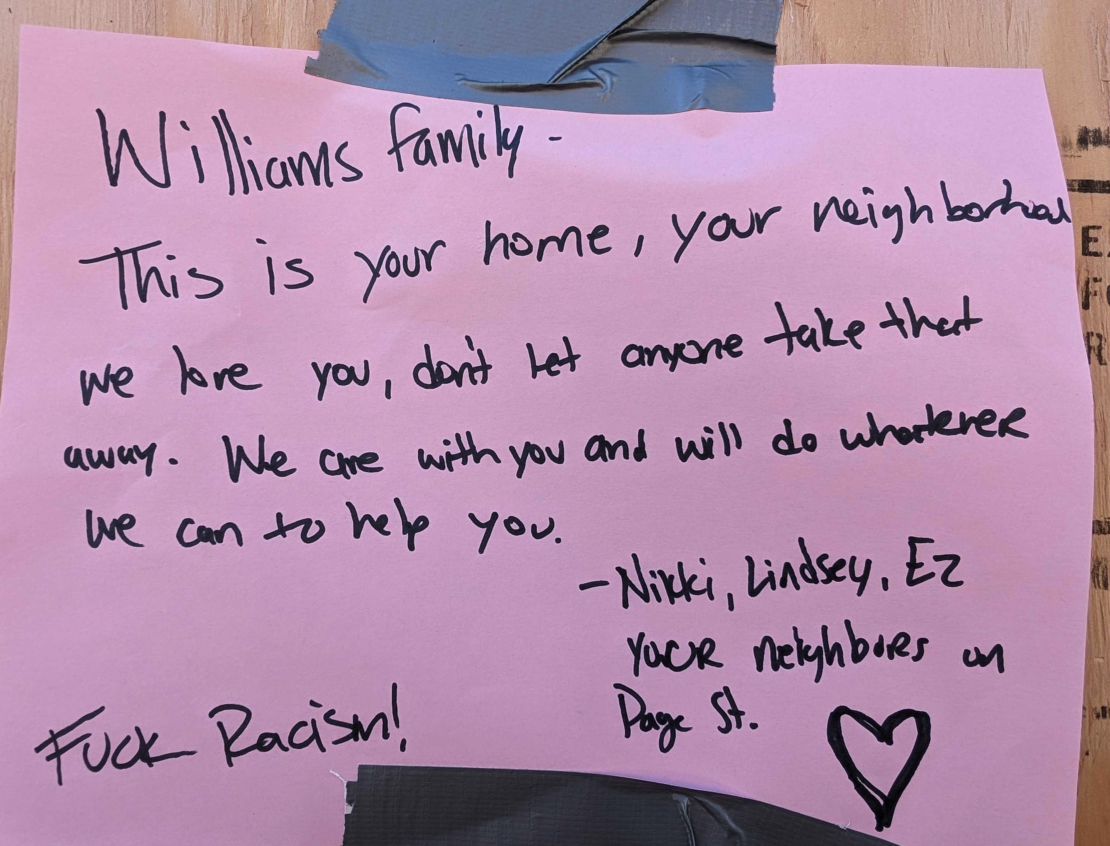 A handwritten note on pink paper taped to a surface expresses support for the Williams family, denounces racism, and is signed by neighbors Nikki, Lindsey, and Ez.