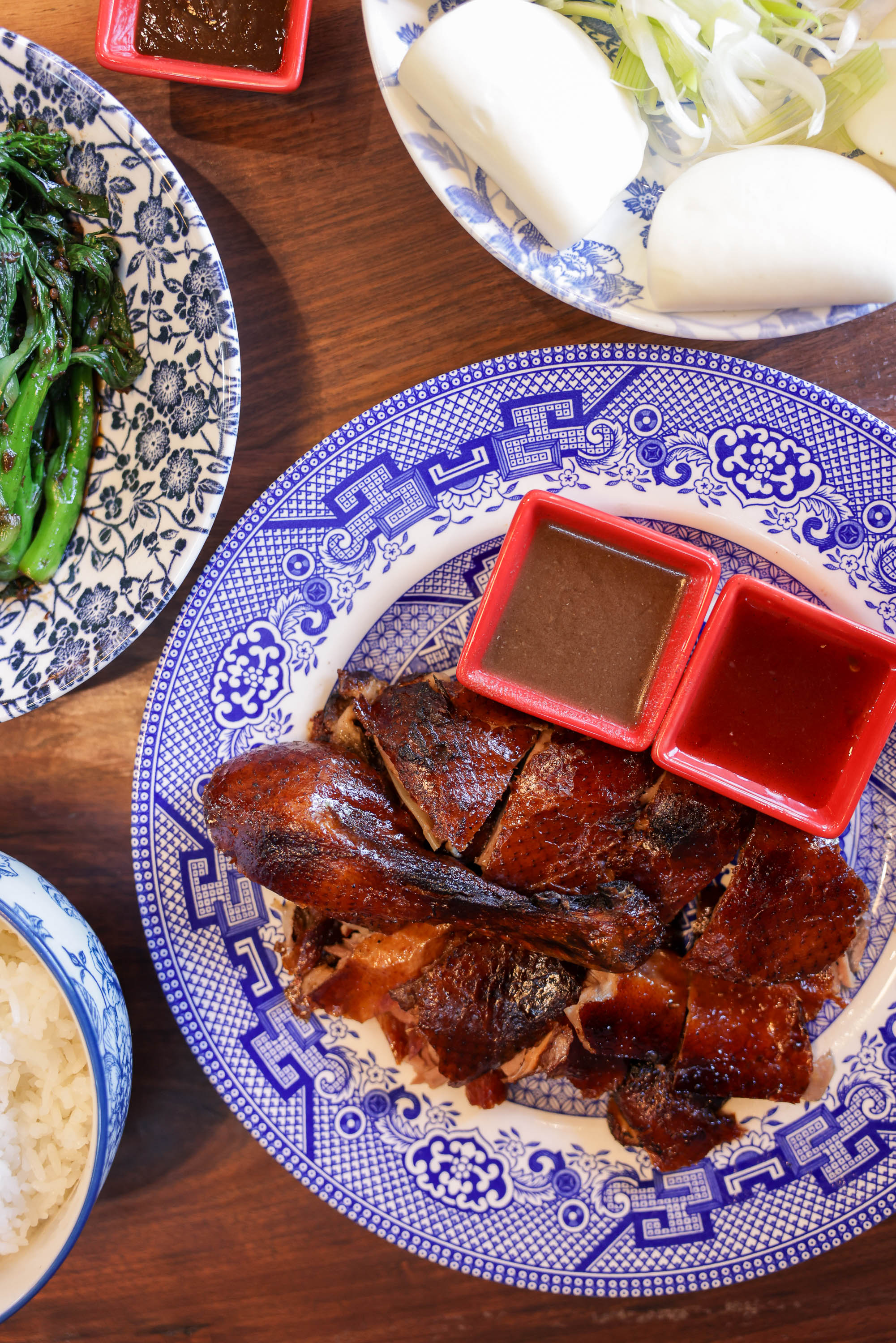 A table with Cantonese duck, steamed buns, green veggies, and sauces on ornate Chinese plates.